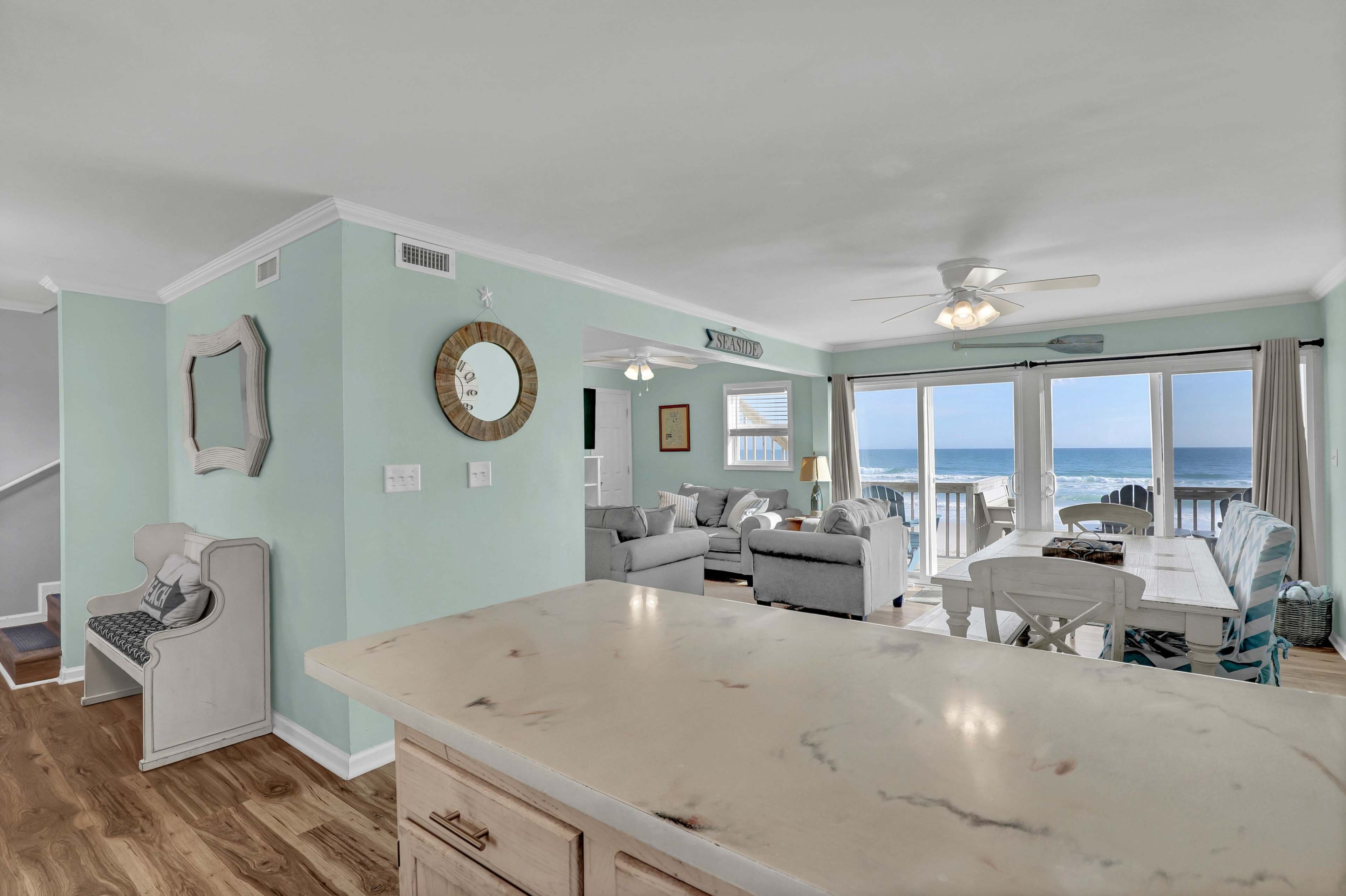 The image shows a bright, spacious living area with a view of the ocean through large glass sliding doors.