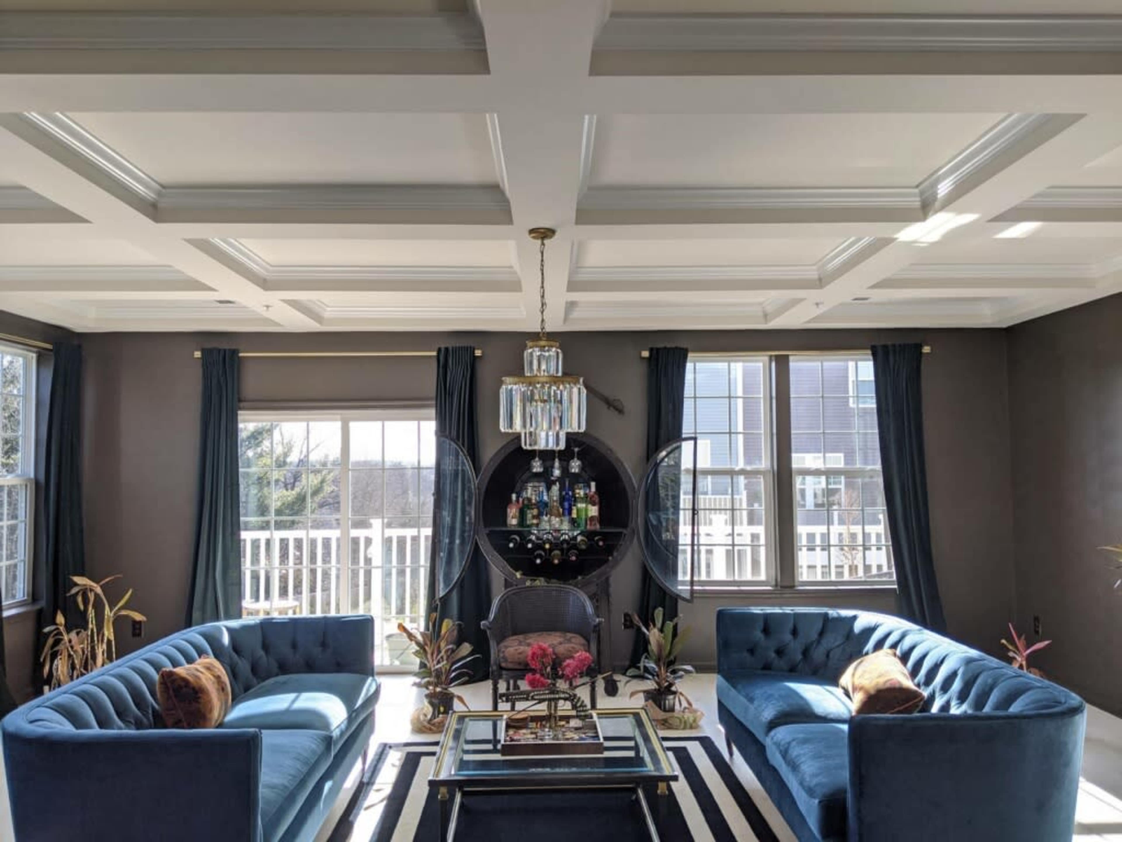 A modern living room featuring two blue sofas facing each other, a glass coffee table with a decorative arrangement, and large windows with sheer curtains.