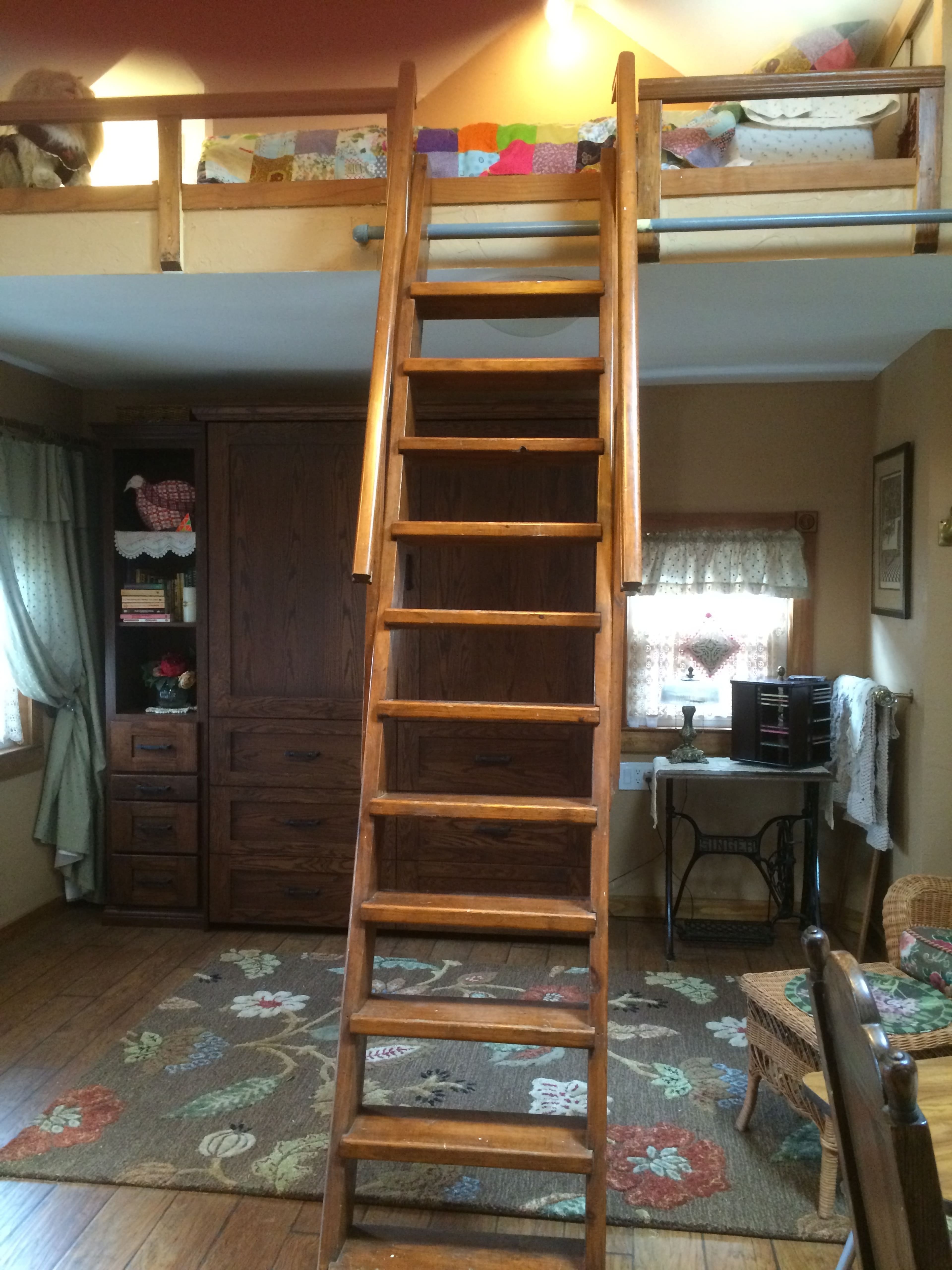 A wooden ladder leads to a loft area above a cozy living space with a rug and various furnishings.