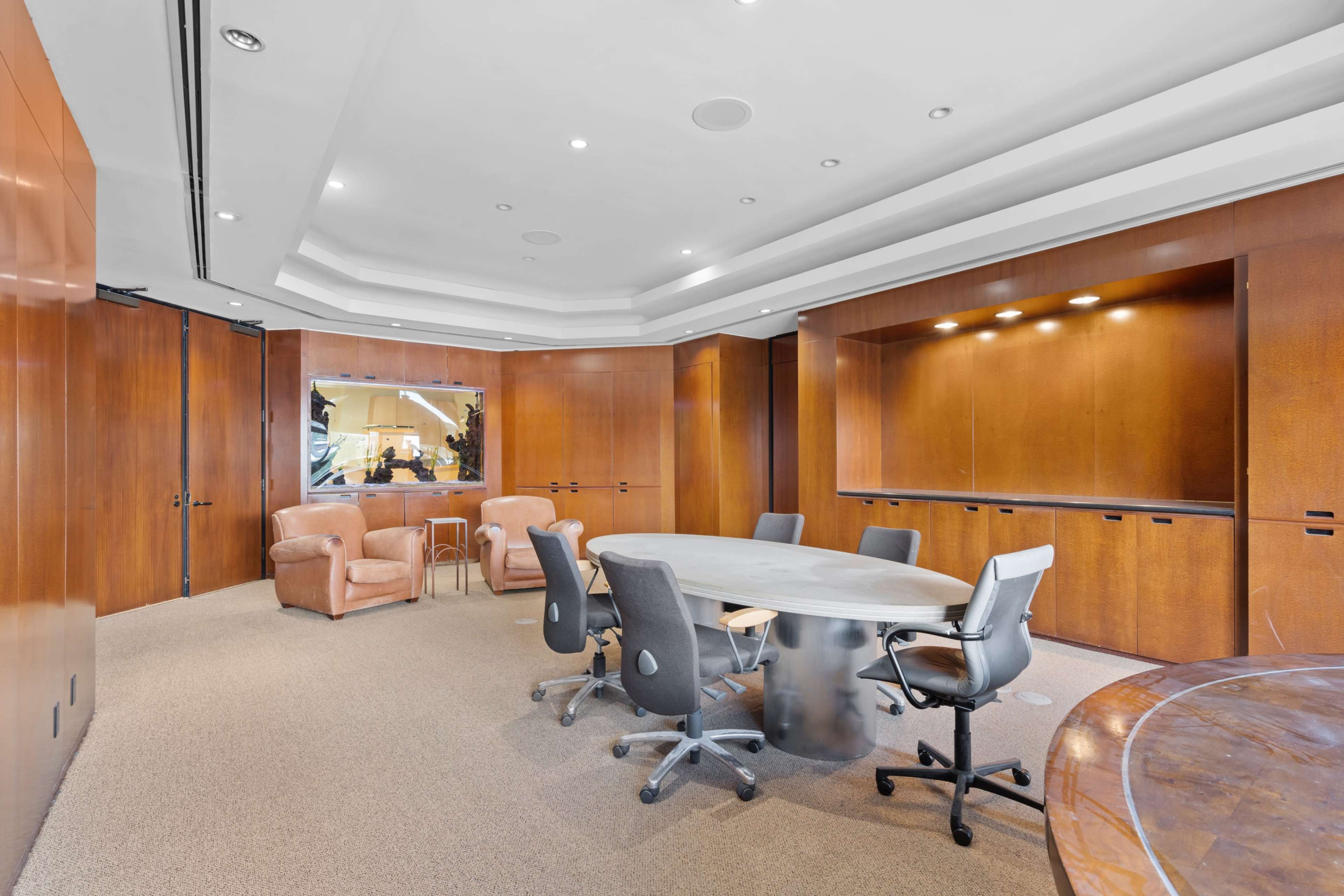 The image shows a modern conference room featuring a round table, several office chairs, and wooden paneling on the walls.
