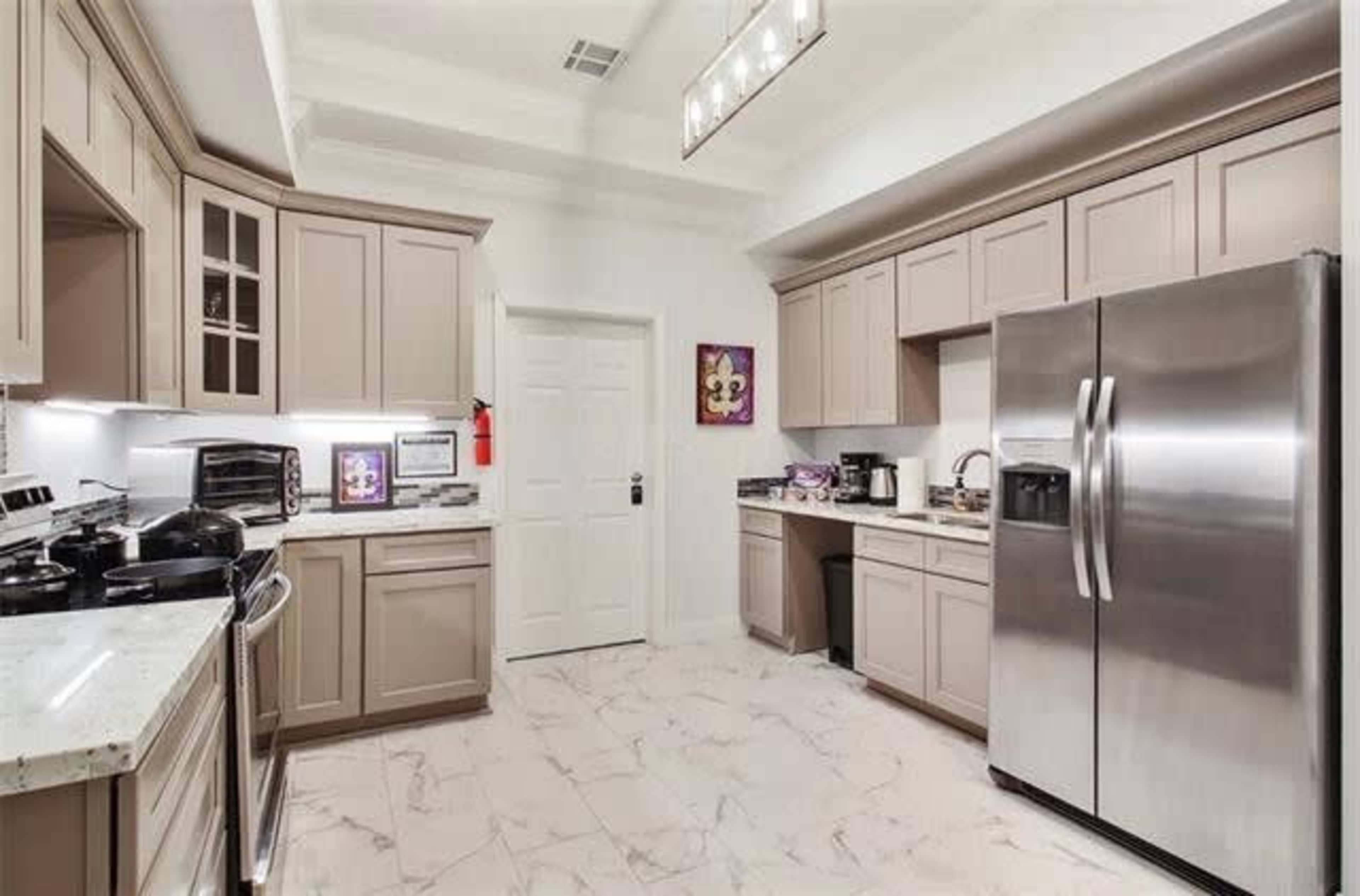 A modern kitchen with light-colored cabinetry, a stainless steel refrigerator, and marble-like tile flooring.