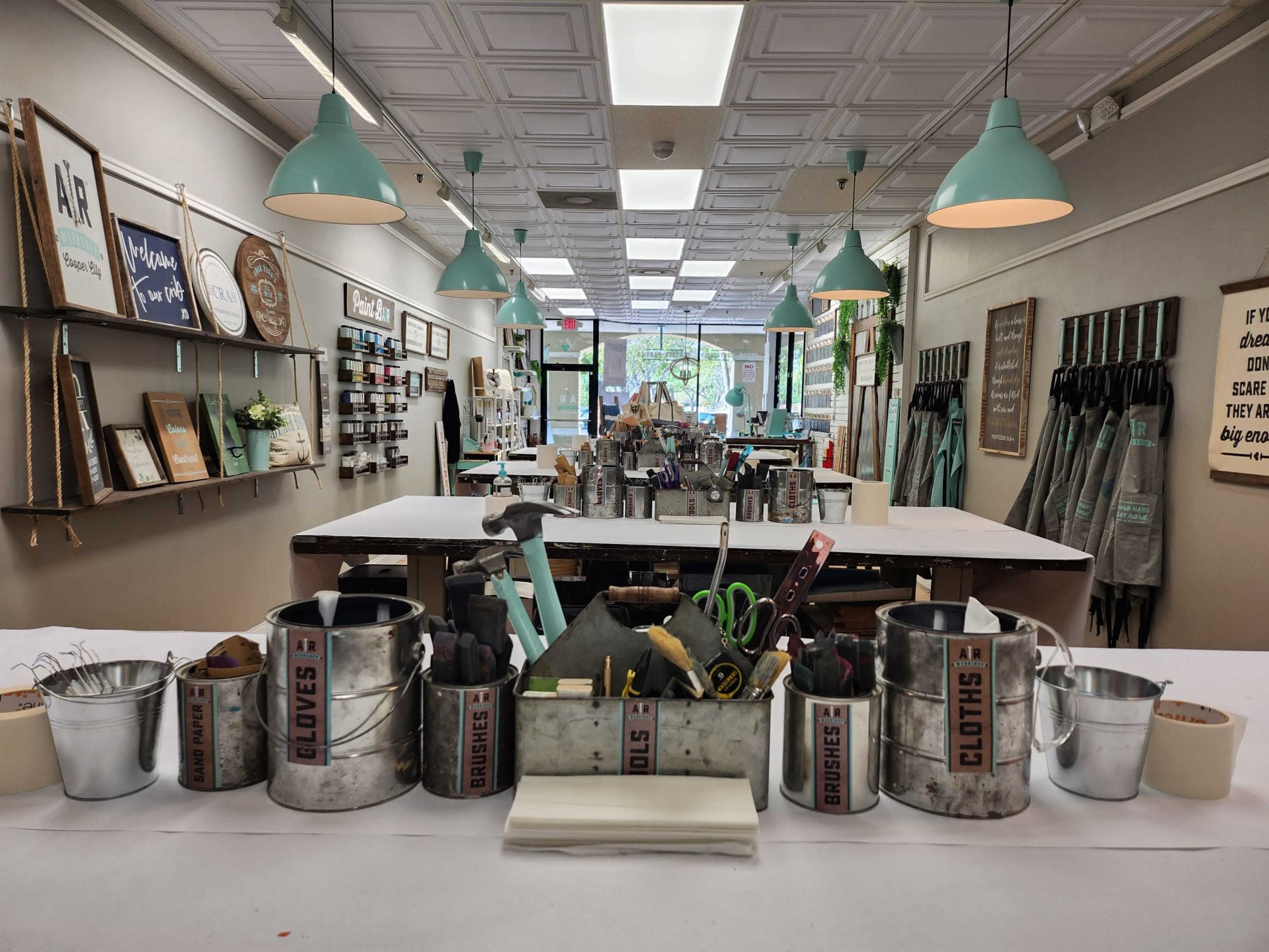 A craft studio with a central table filled with various tools and supplies, surrounded by decorated walls and organized workspaces.