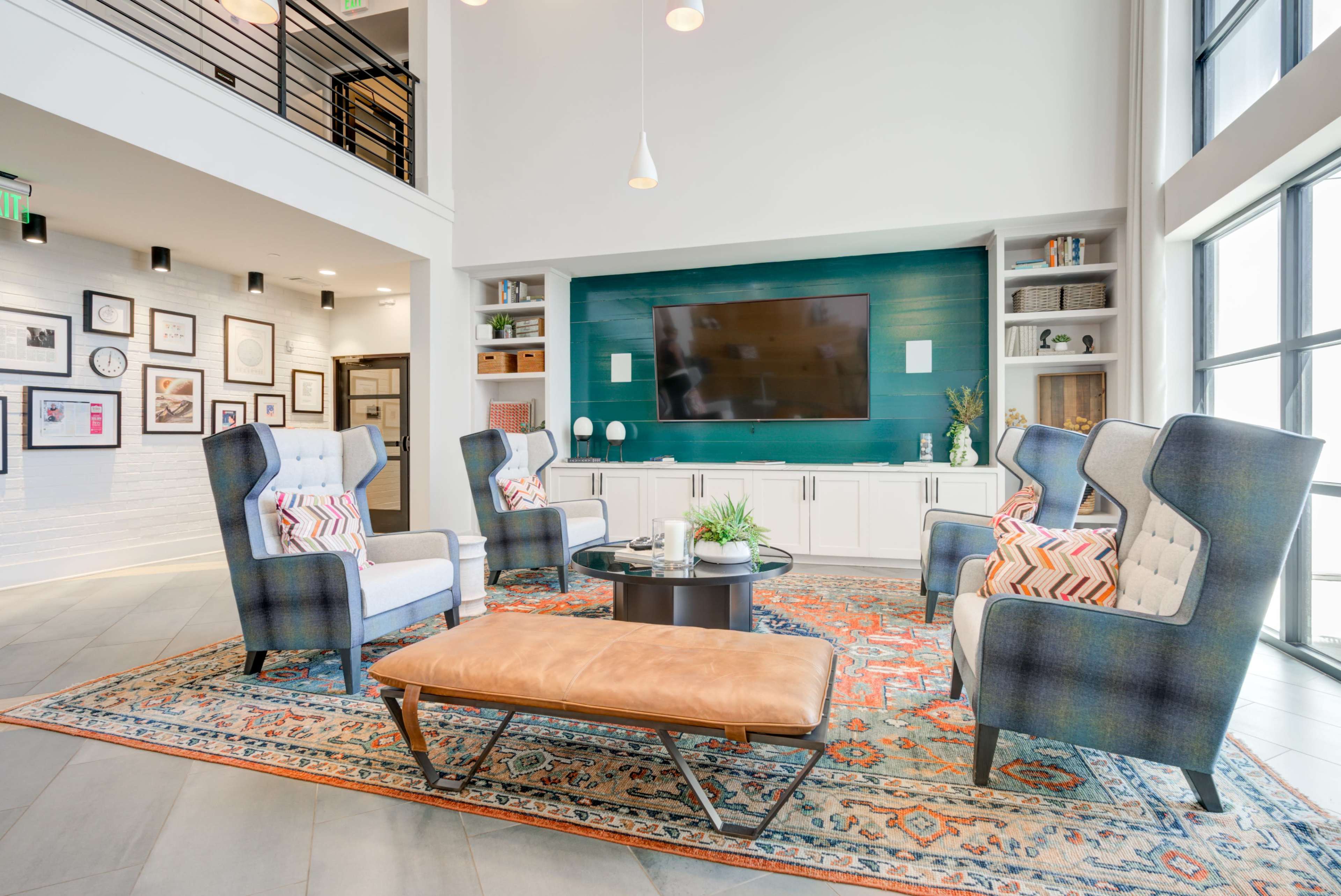 A modern living area featuring four patterned chairs arranged around a circular coffee table on a decorative rug, with a large television mounted on a wall and shelves displaying decor.