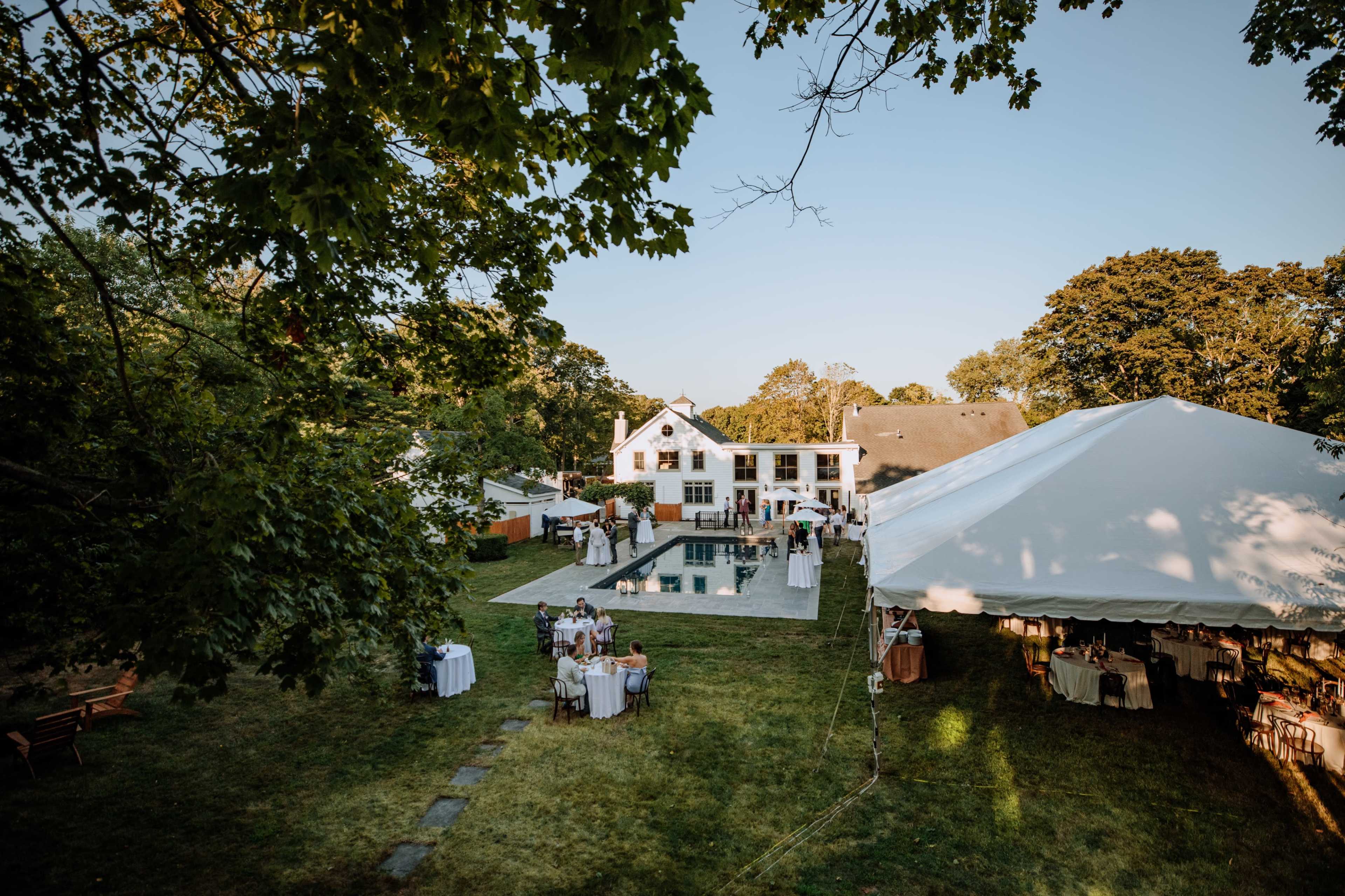 A spacious backyard features a large swimming pool surrounded by a tented area and tables for an outdoor event.