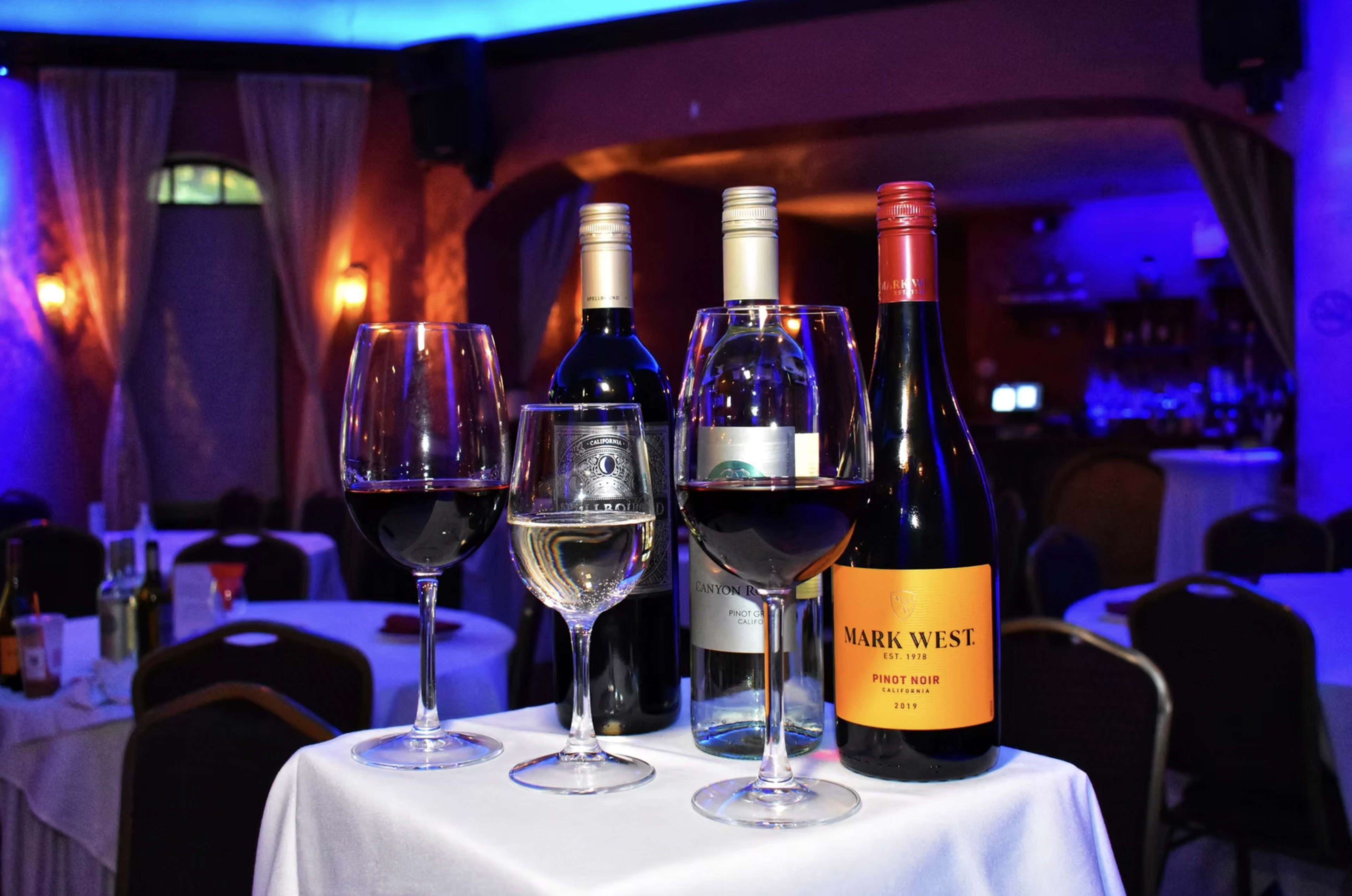 The image shows a table with four wine glasses and bottles of red and white wine, set in a dimly lit restaurant with blue lighting.