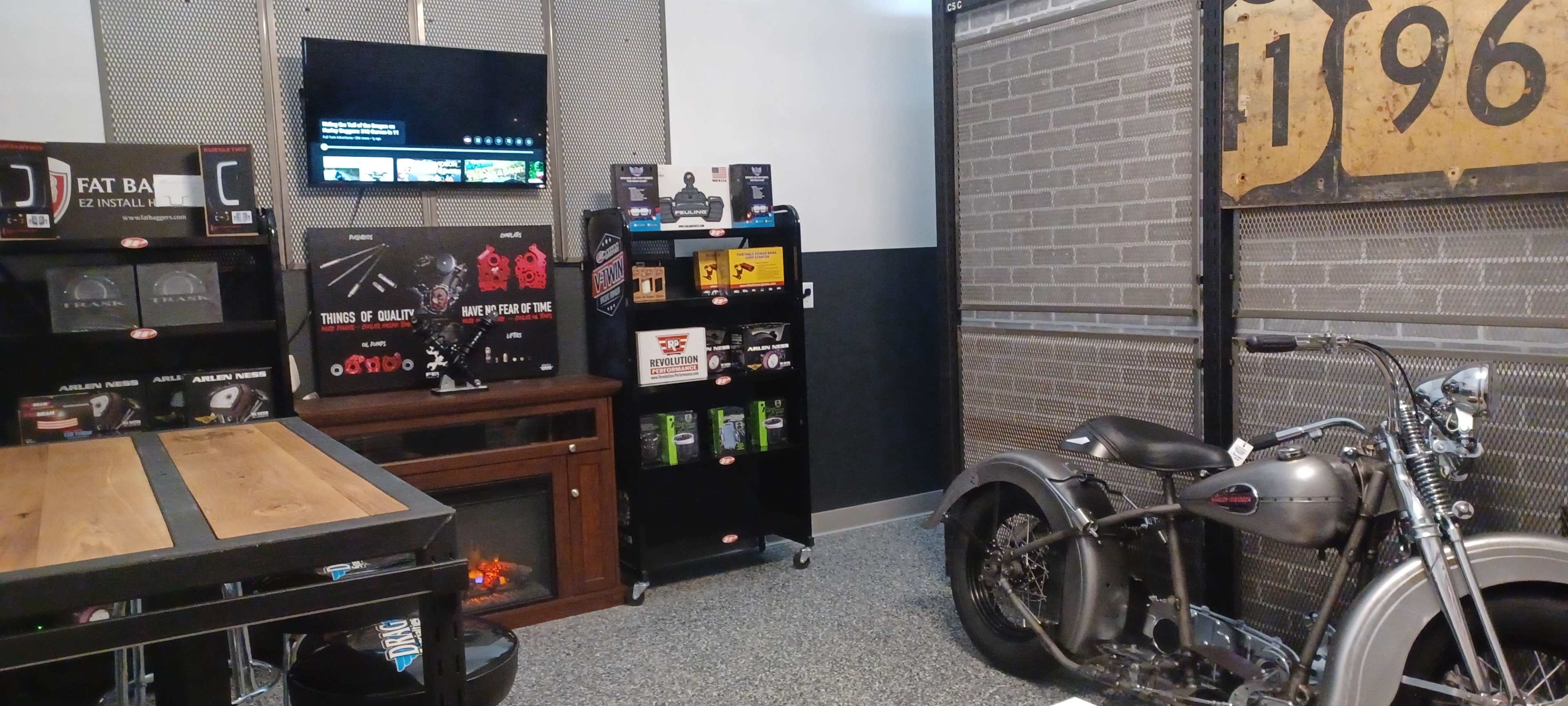 A display area featuring motorcycle accessories and a vintage motorcycle beside a television and decorative signage.
