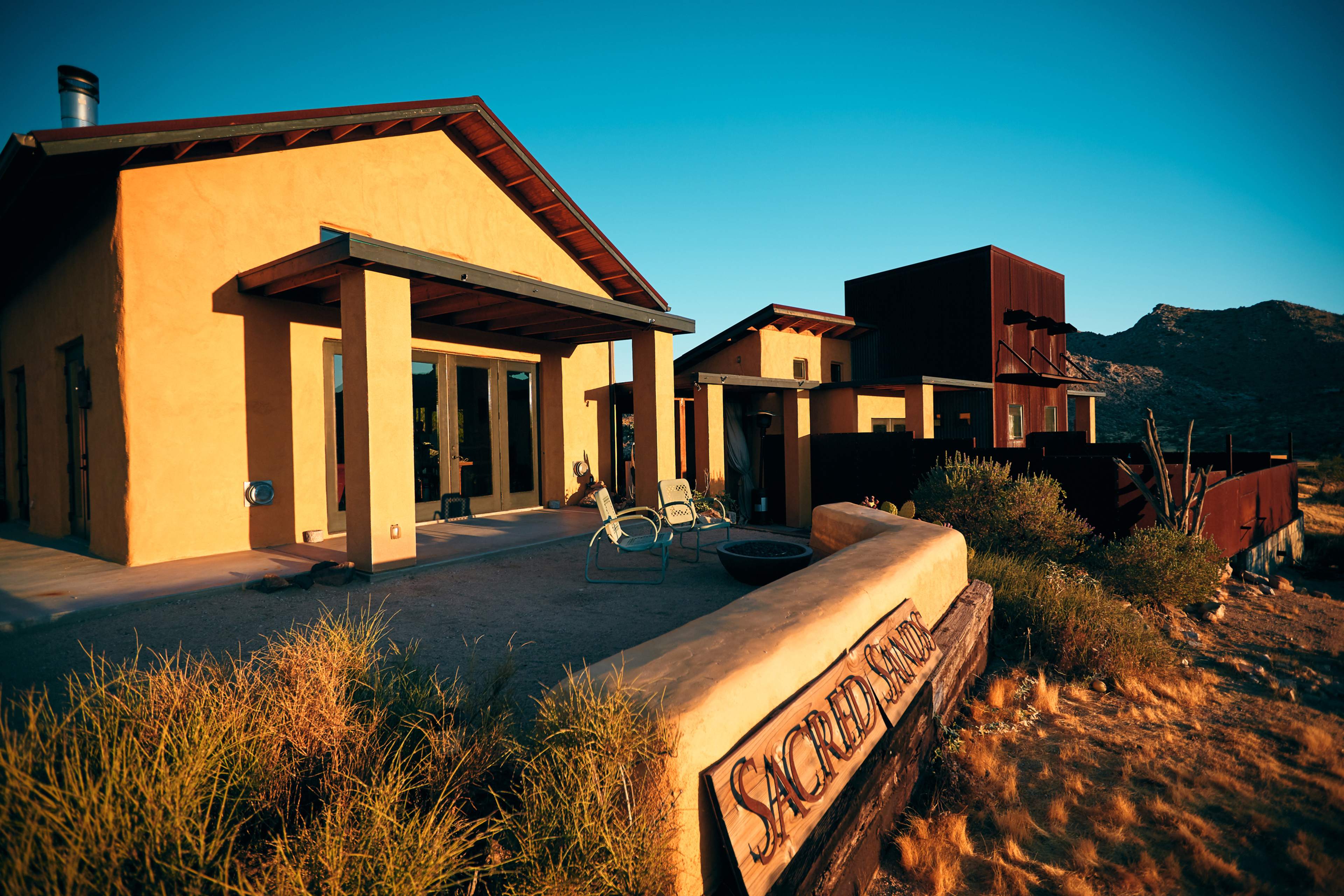A modern adobe-style building with a wooden sign labeled "Sacred Site" in a rural desert landscape.