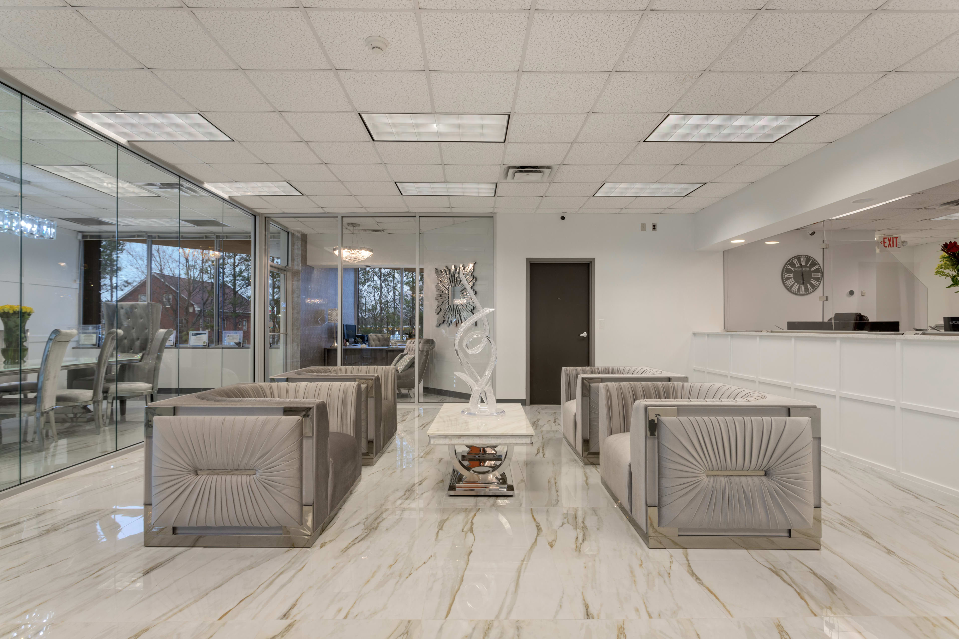 A modern reception area with marble flooring, gray seating, and a glass-walled meeting room in the background.