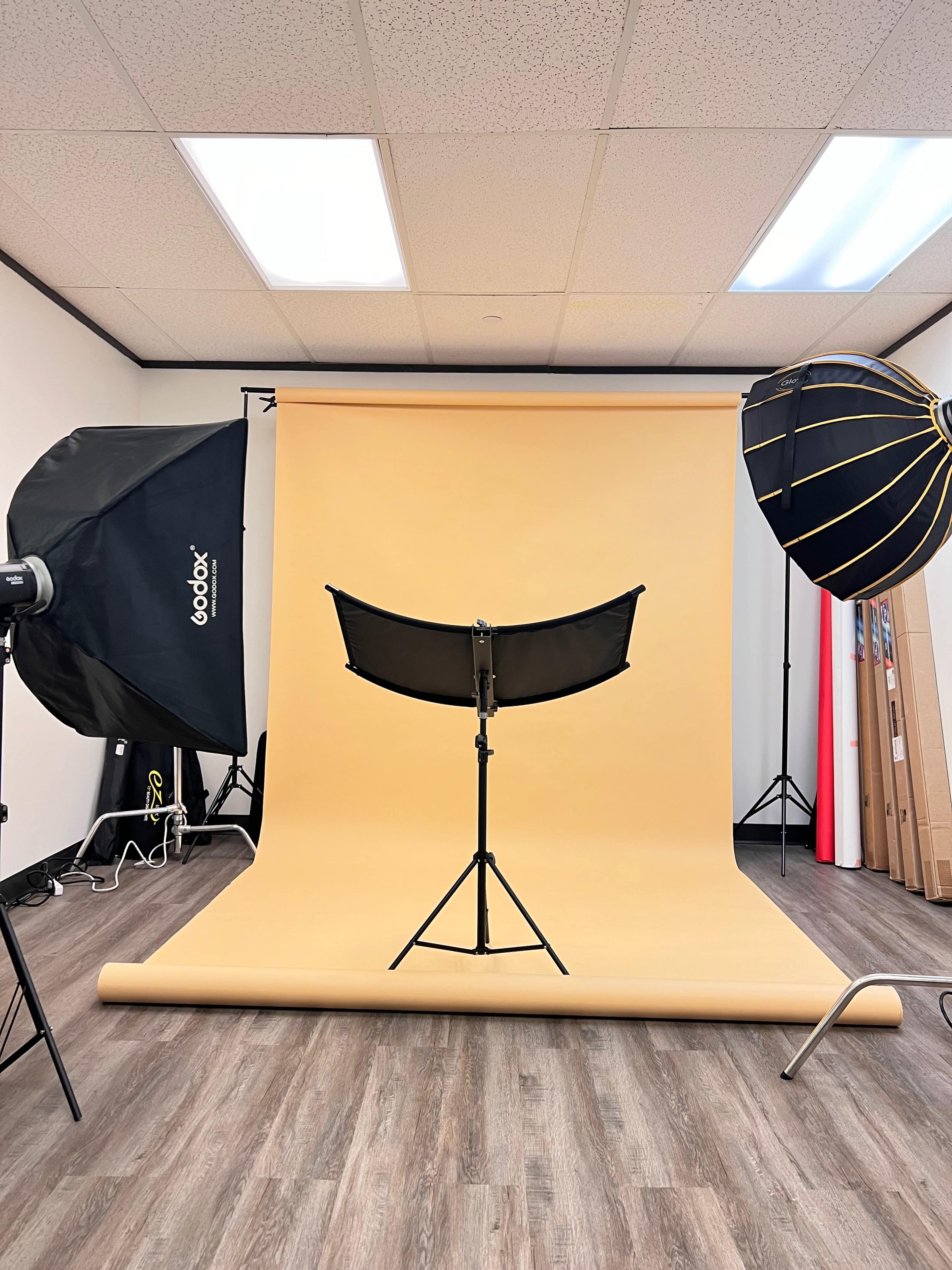 A photography studio features a yellow backdrop, lighting equipment, and a stand positioned in the center.