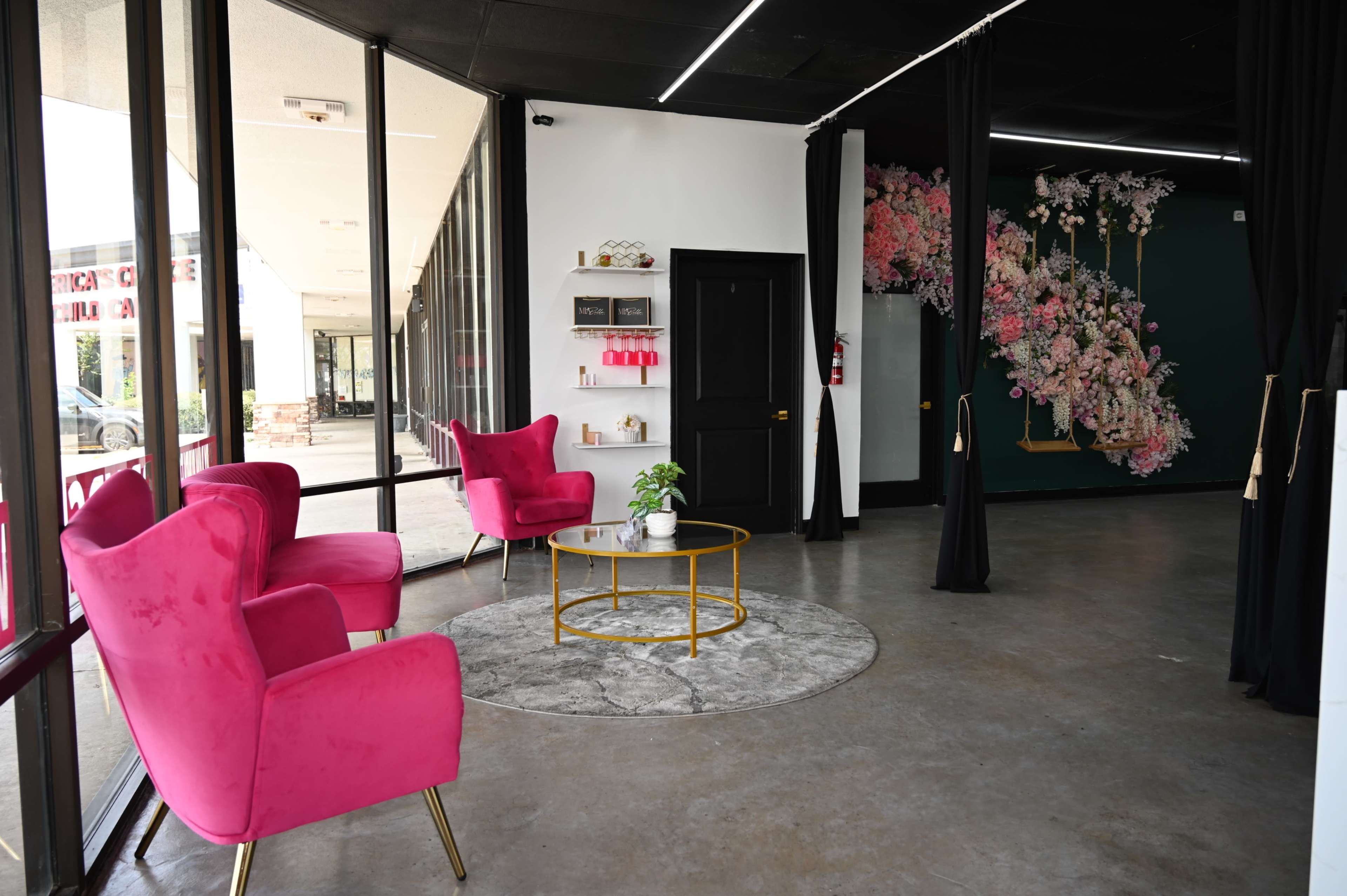 A modern interior features two pink armchairs, a round gold coffee table, and a decorative wall with floral designs.