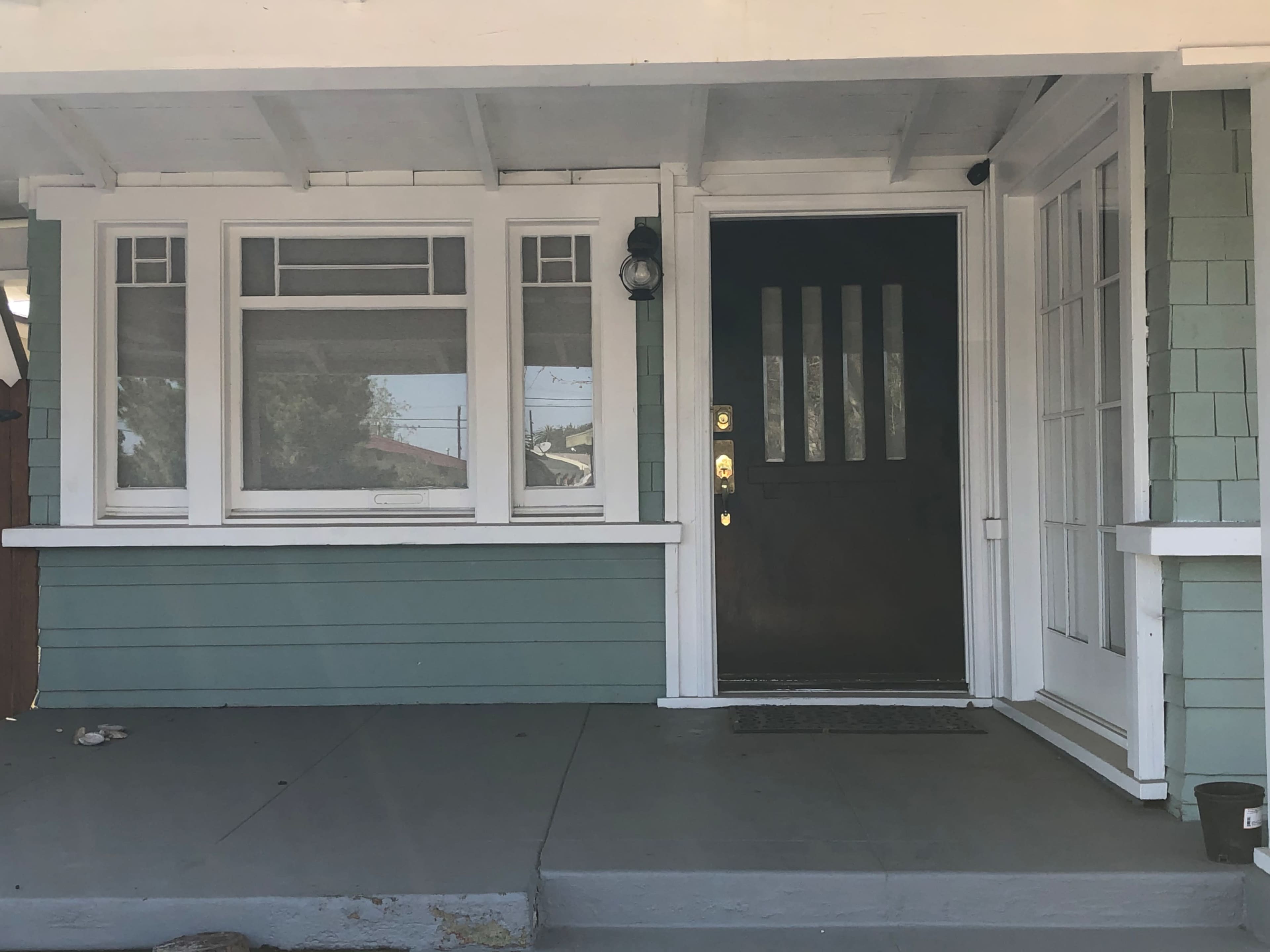 The image shows a house entryway with a dark front door, large side windows, and green vertical siding.