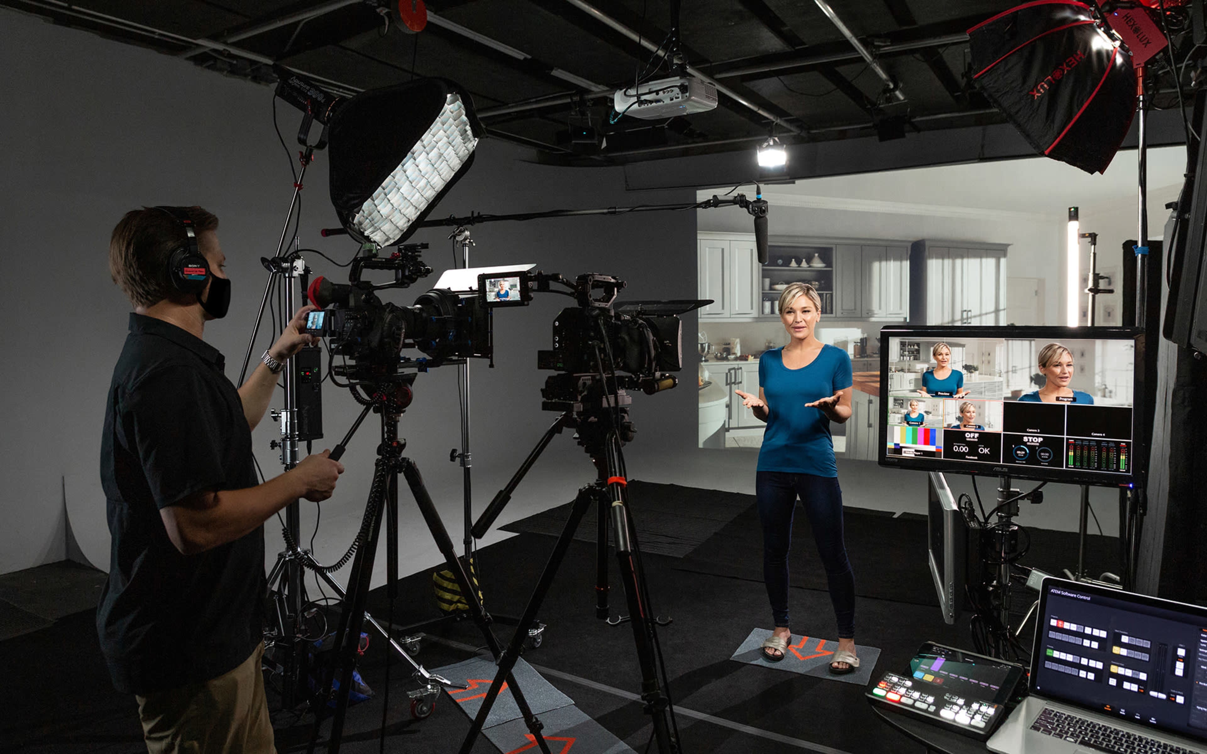 A person is filming in a studio setup with multiple cameras and lighting equipment, while a presenter stands in front of a screen displaying a kitchen background.
