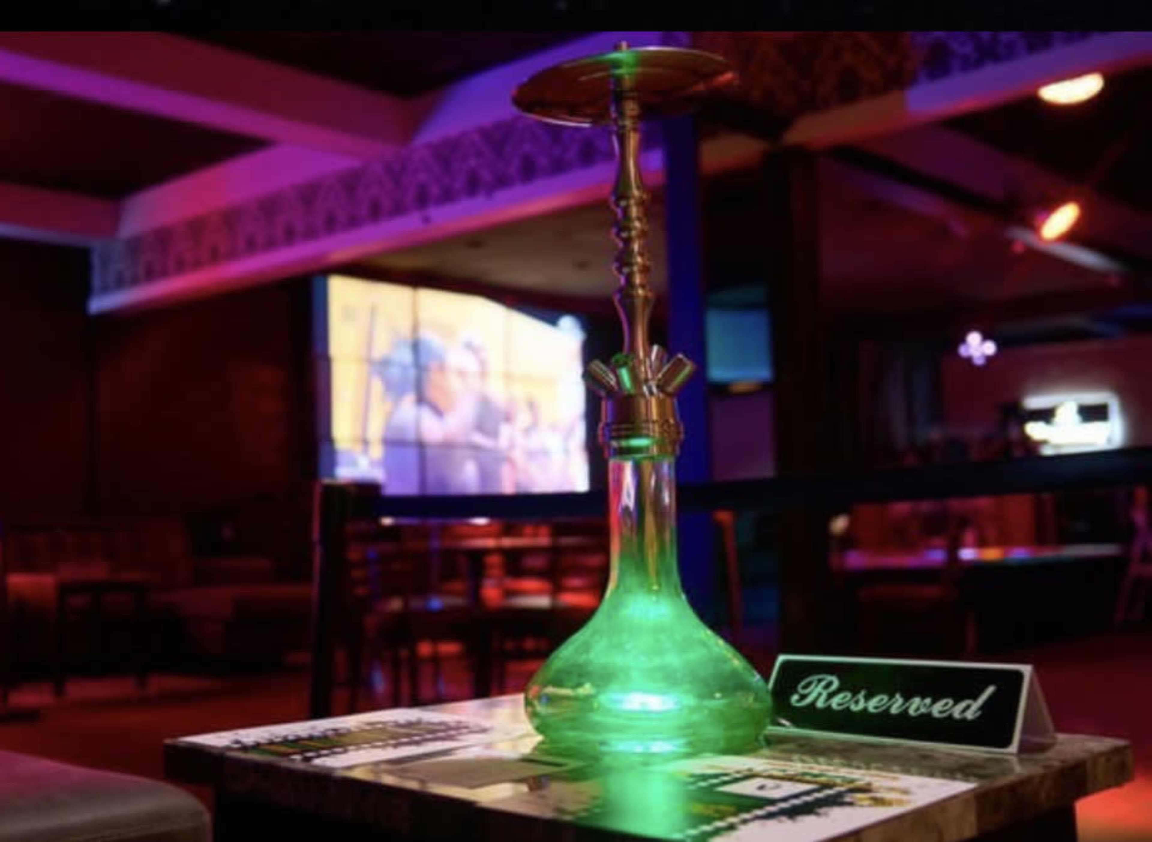 A lit hookah is placed on a table marked "Reserved" in a dimly lit lounge with a projection screen in the background.