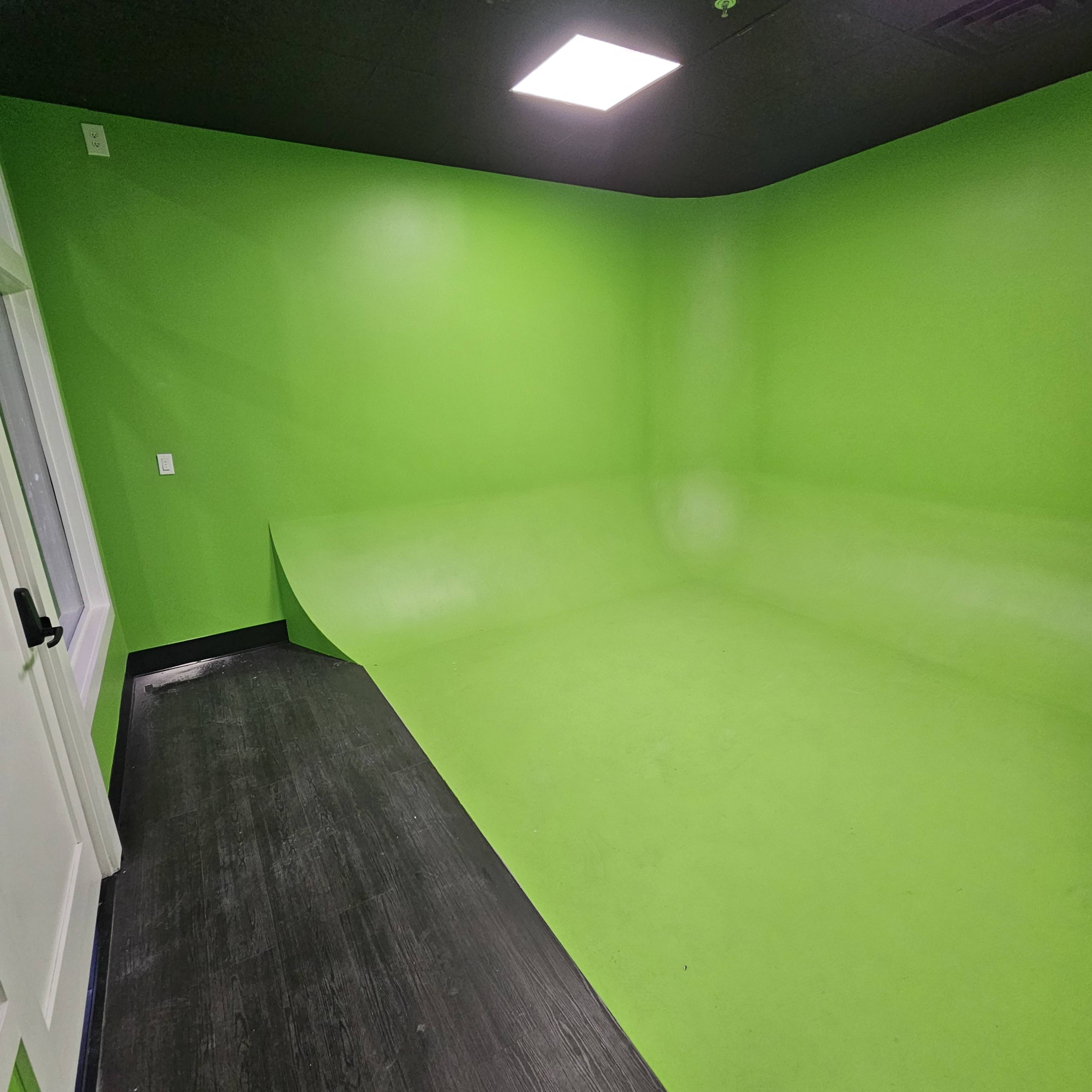 The image shows a bright green room with a seamless floor and walls, designed for video production or photography.
