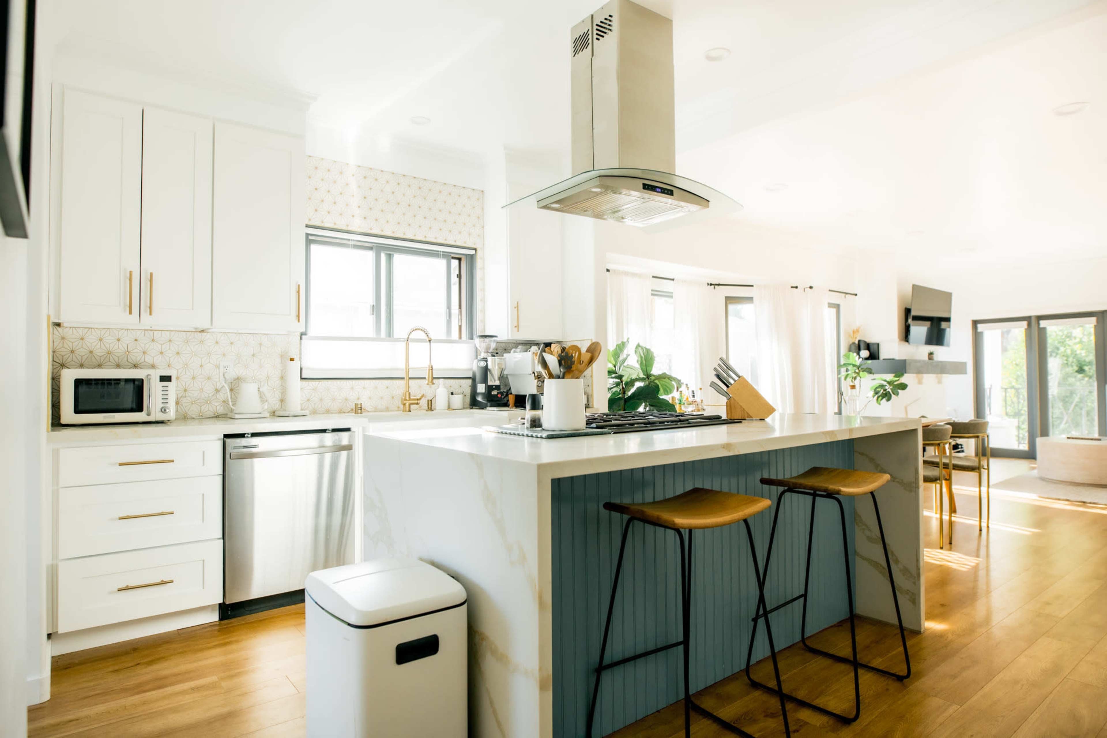A modern kitchen features a center island with bar stools, stainless steel appliances, and light wood flooring.
