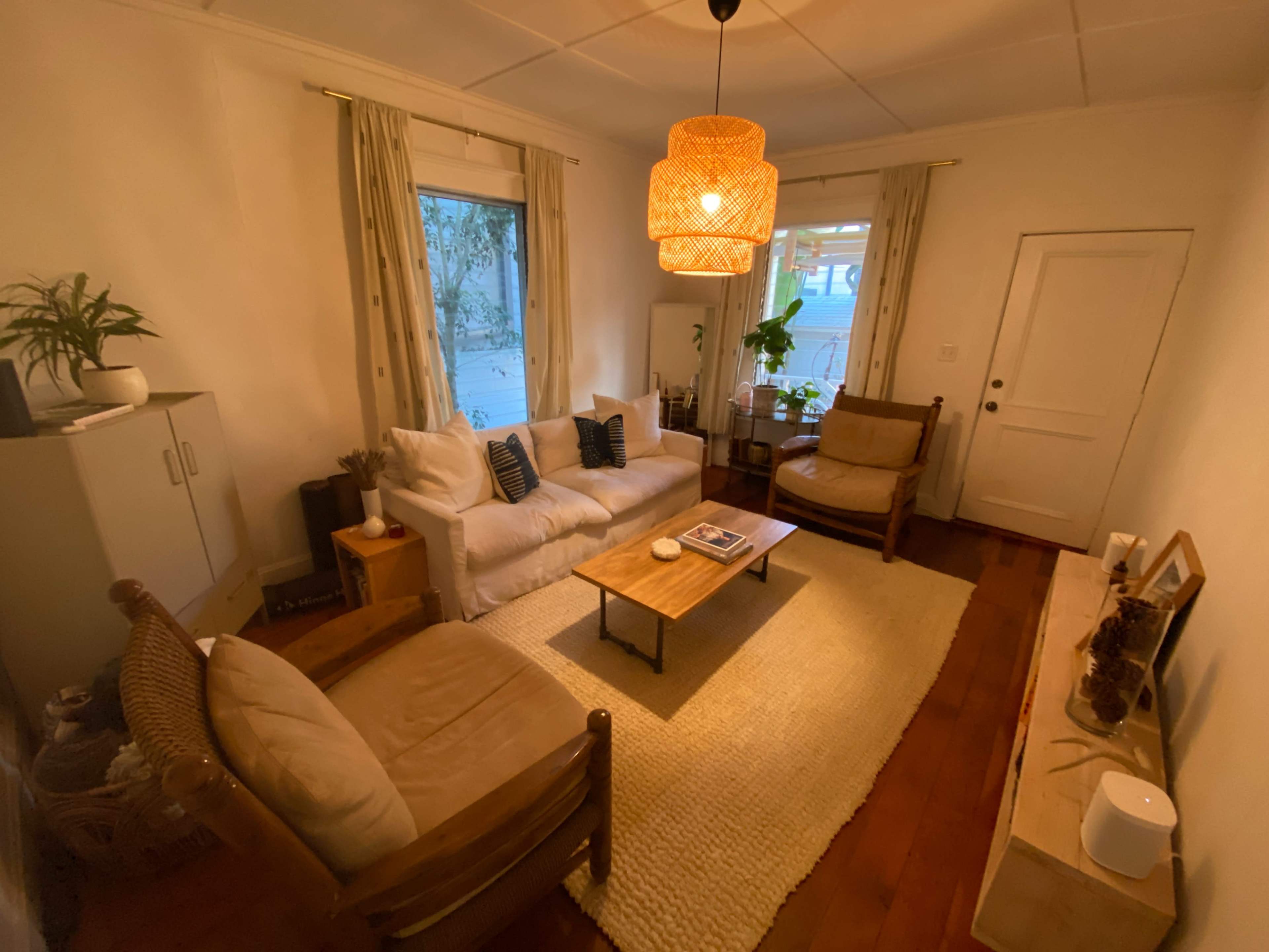 The image shows a cozy living room with a white sofa, two armchairs, a coffee table, and a woven area rug, illuminated by a pendant light.
