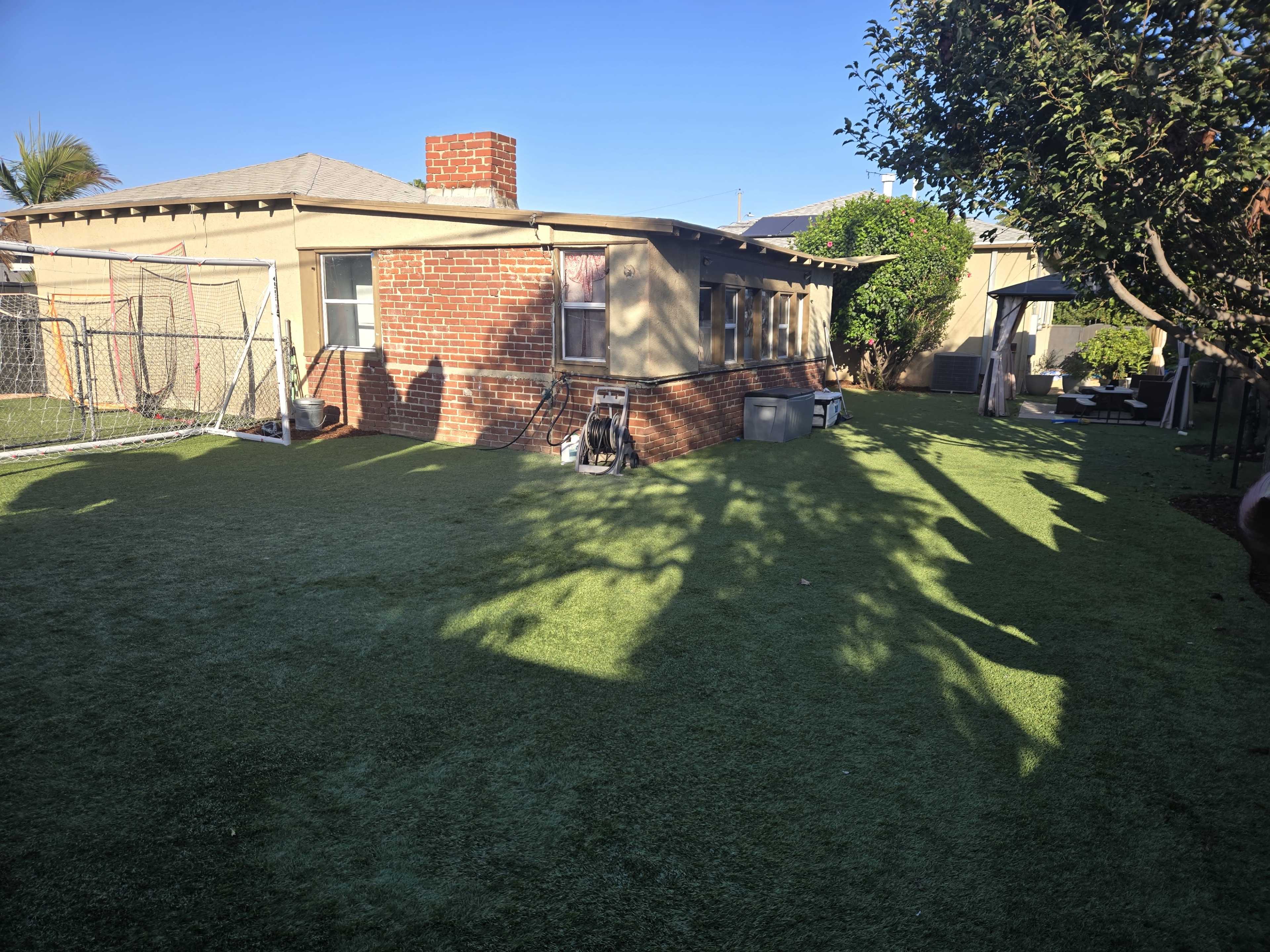 The image shows a backyard with artificial turf, a brick house, a chimney, and a goalpost in the corner.