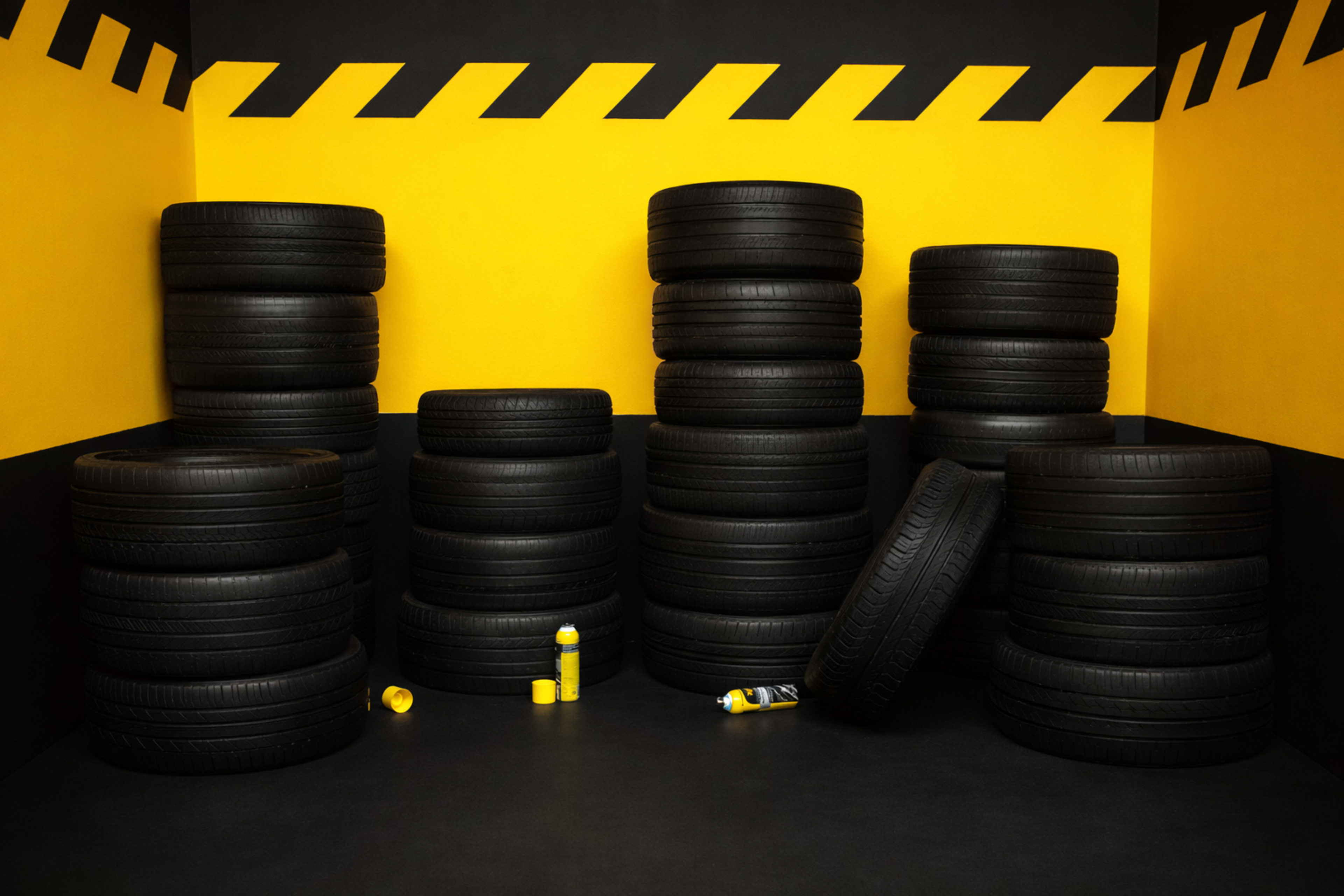 The image features several stacks of black tires arranged in a corner of a room with yellow and black striped walls.