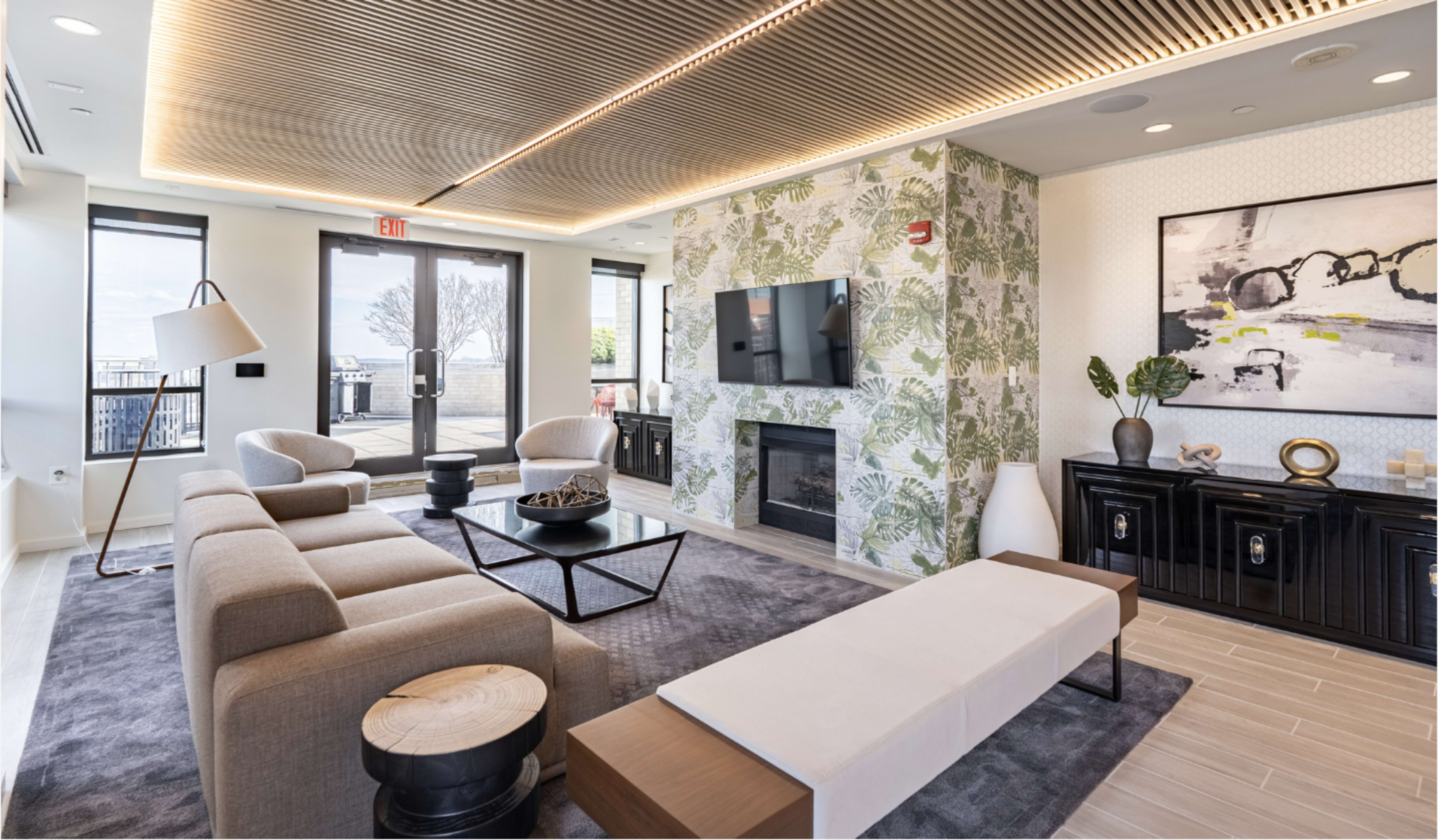 The image shows a modern lounge area with a sofa, chairs, a coffee table, a flat-screen TV, and a decorative wall featuring plants.