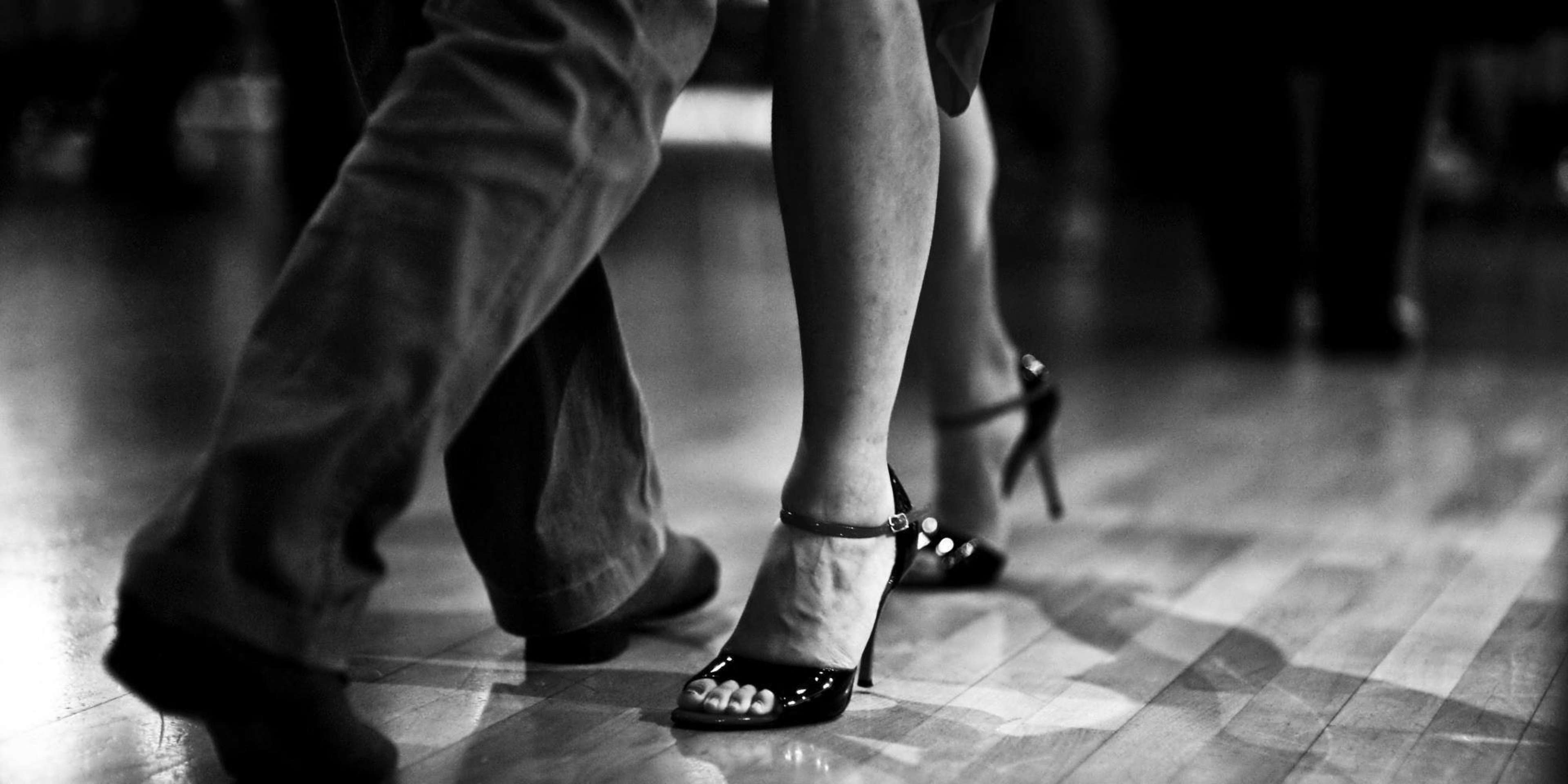 A close-up of two pairs of feet engaged in dancing on a wooden floor.