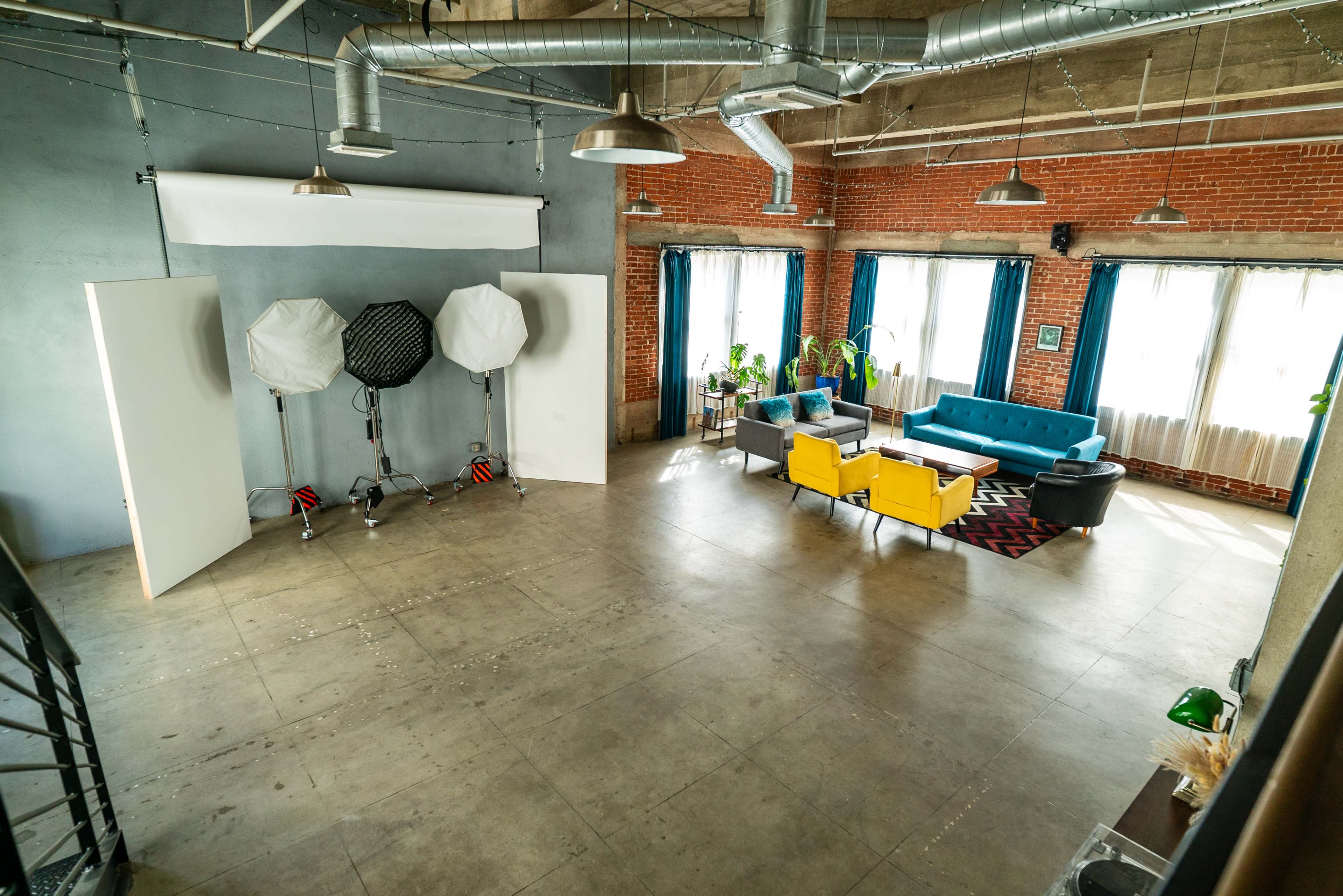 The image shows a well-lit, spacious studio with a modern seating area and photography equipment set up in one corner.