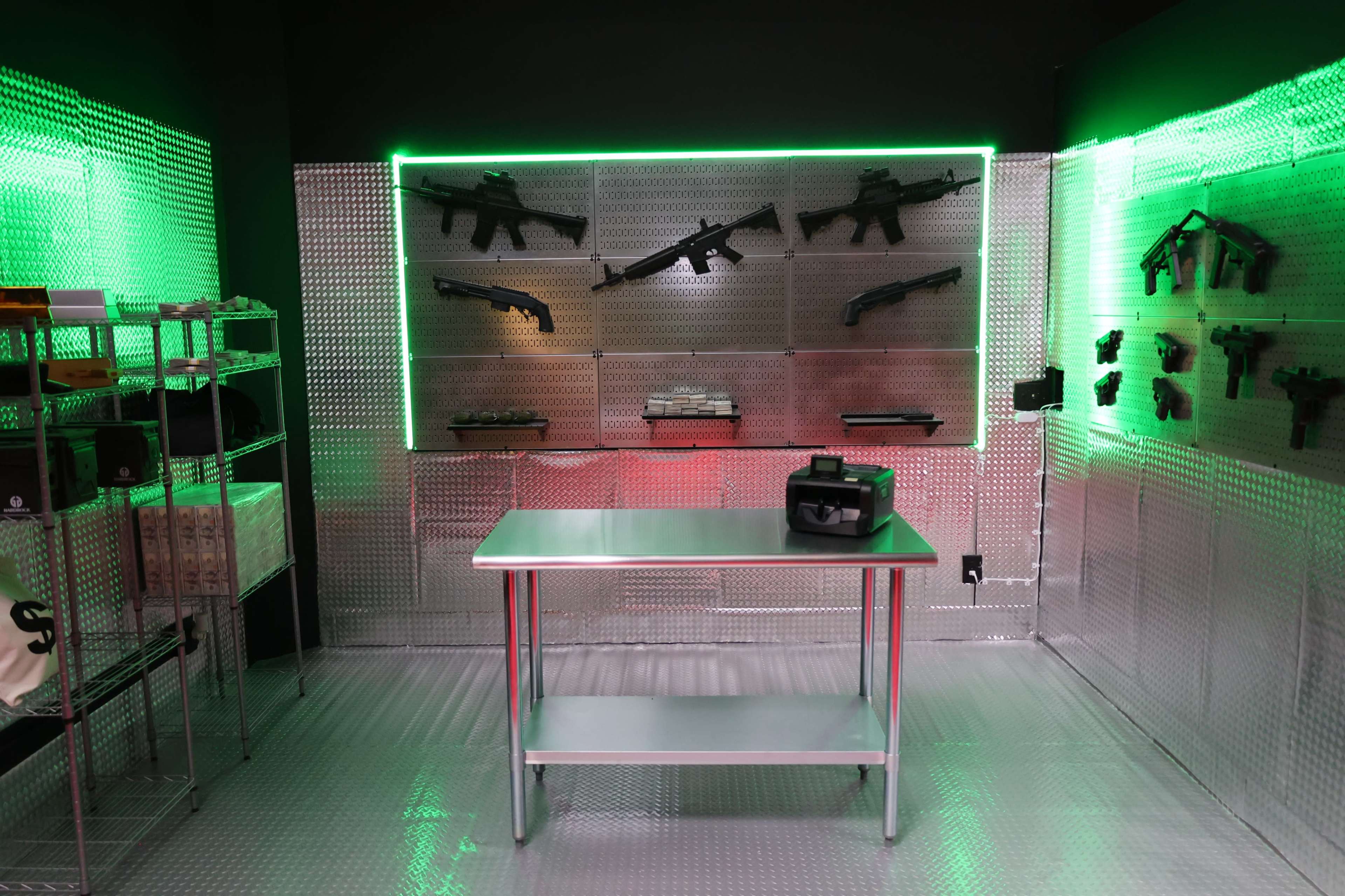 A room with a metallic wall displaying various firearms, illuminated by green and red LED lights, with a stainless steel table in the center.
