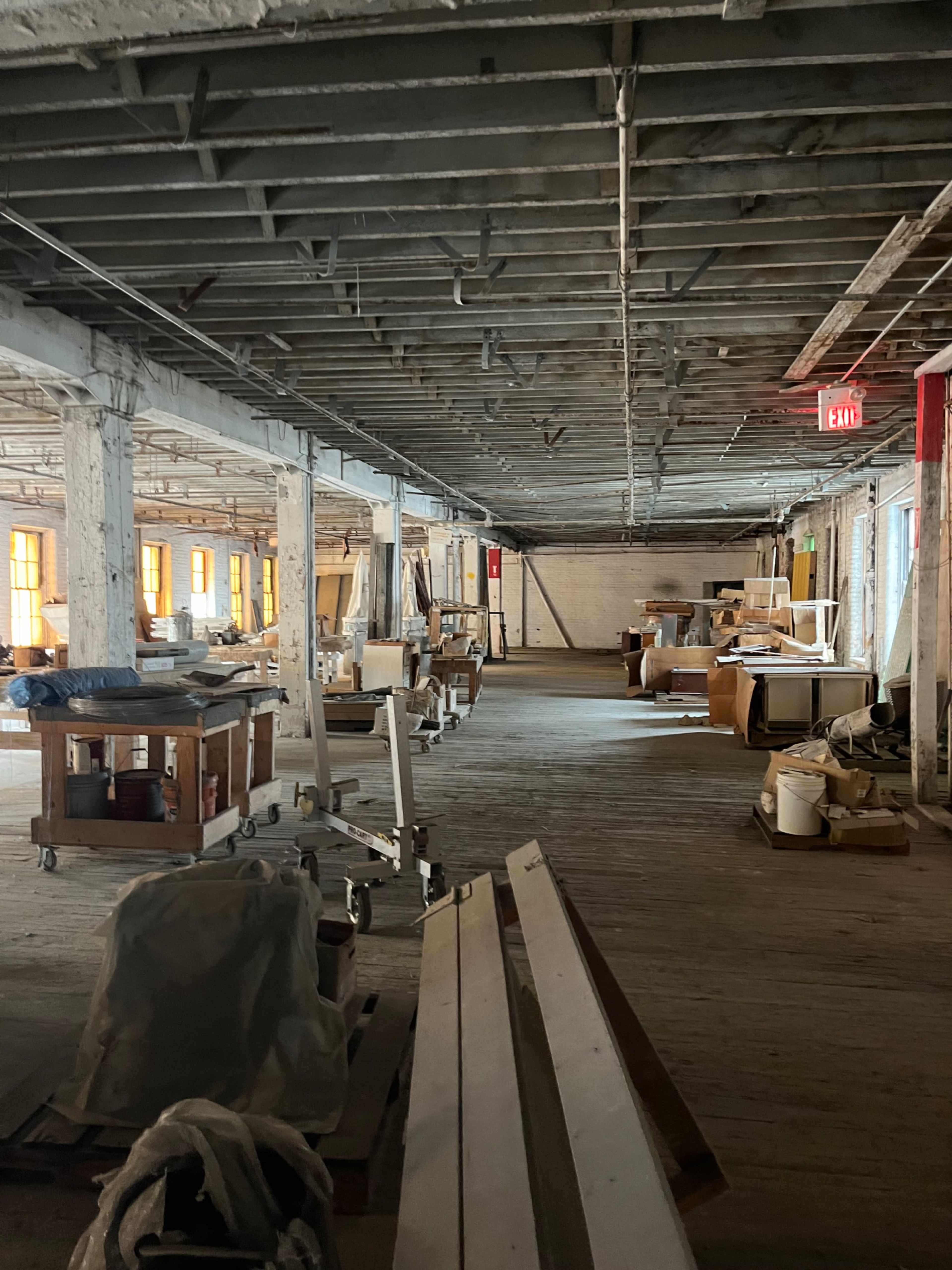 The image shows a spacious, dimly lit warehouse interior with various wooden carts and stacks of materials arranged along the sides.