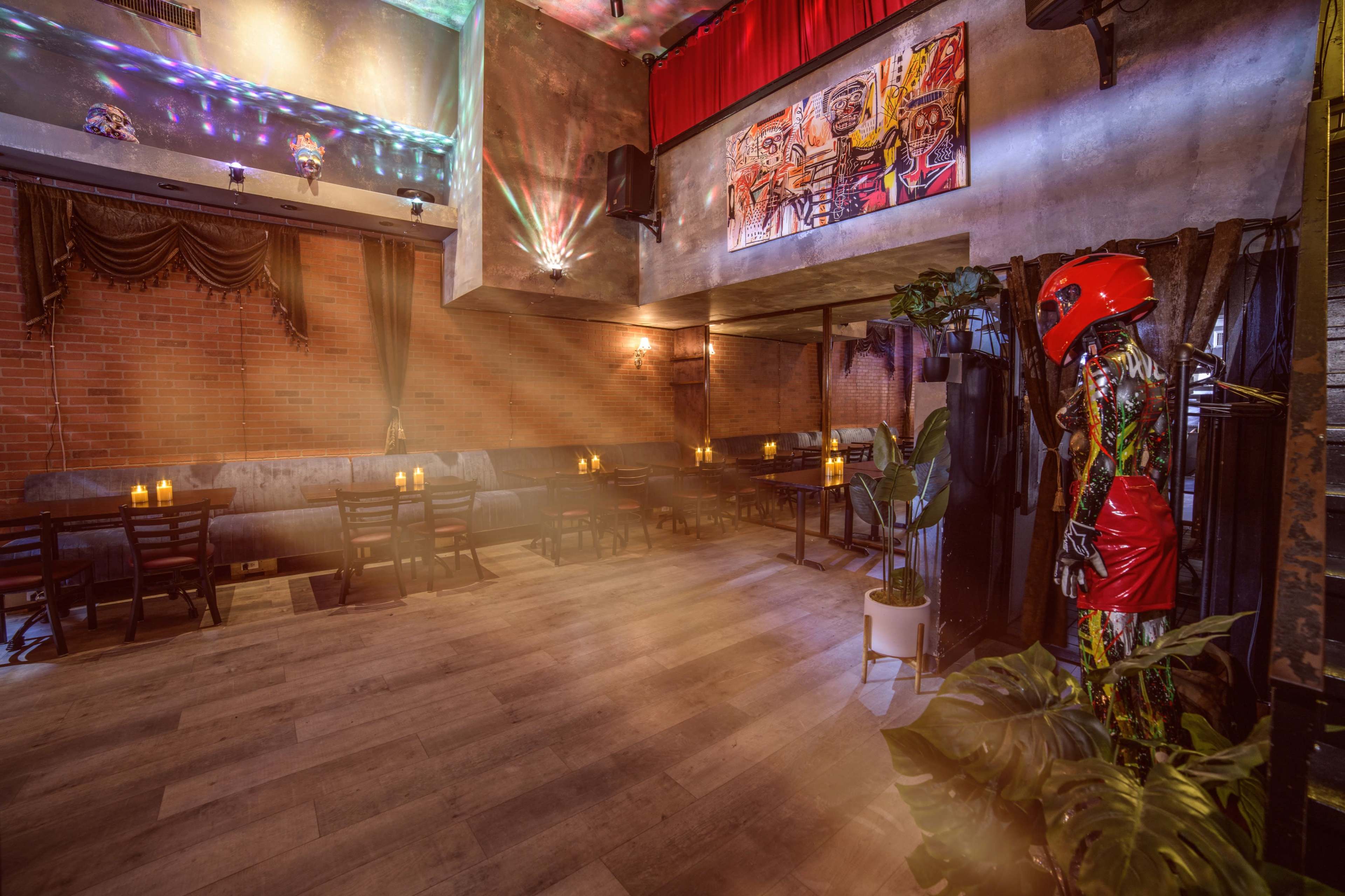 The image shows an indoor venue with wooden tables and chairs, decorated with dim lighting and colorful art on the walls.