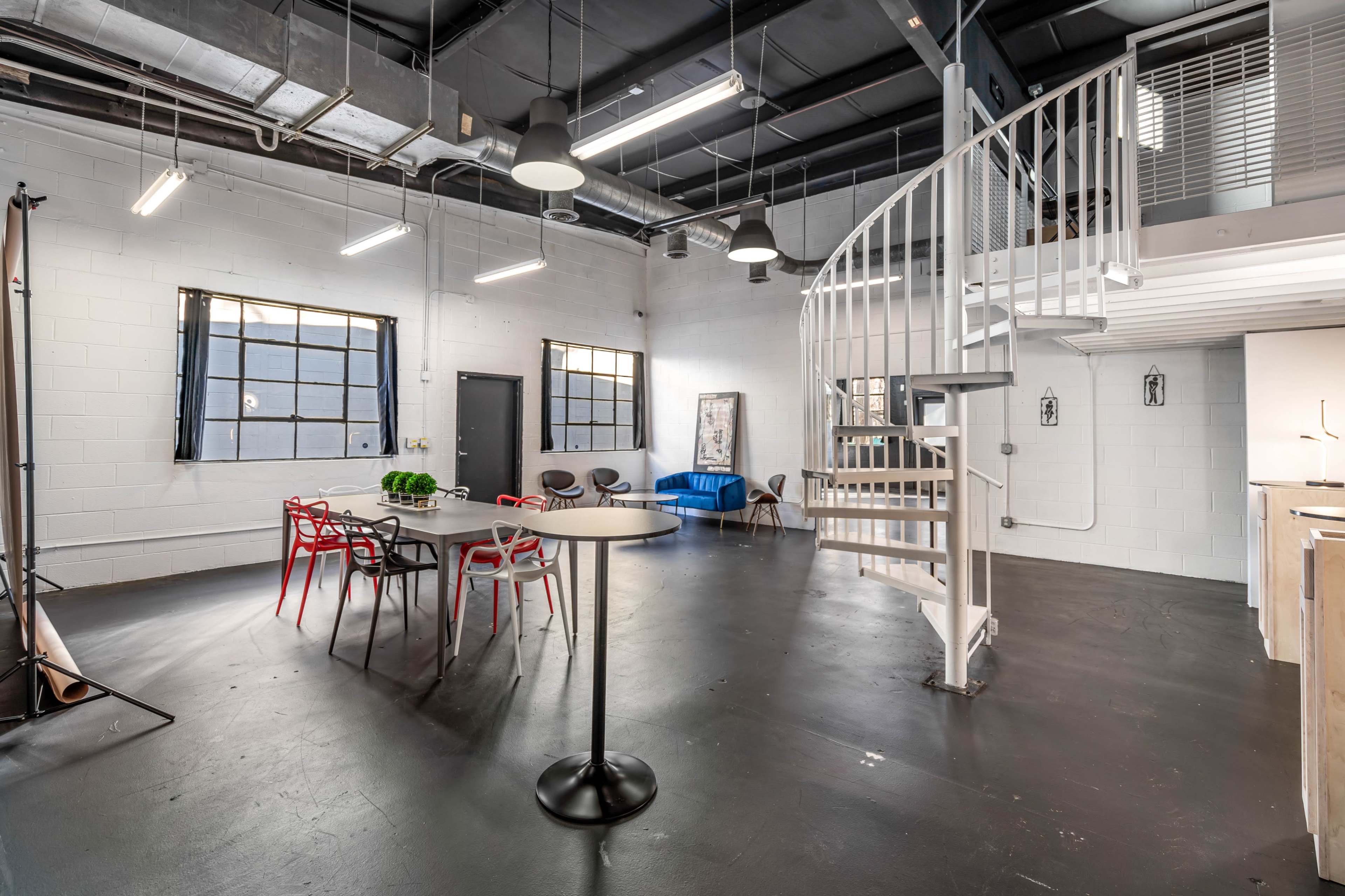 A spacious industrial-style room with a spiral staircase, multiple windows, and a mix of modern furniture.