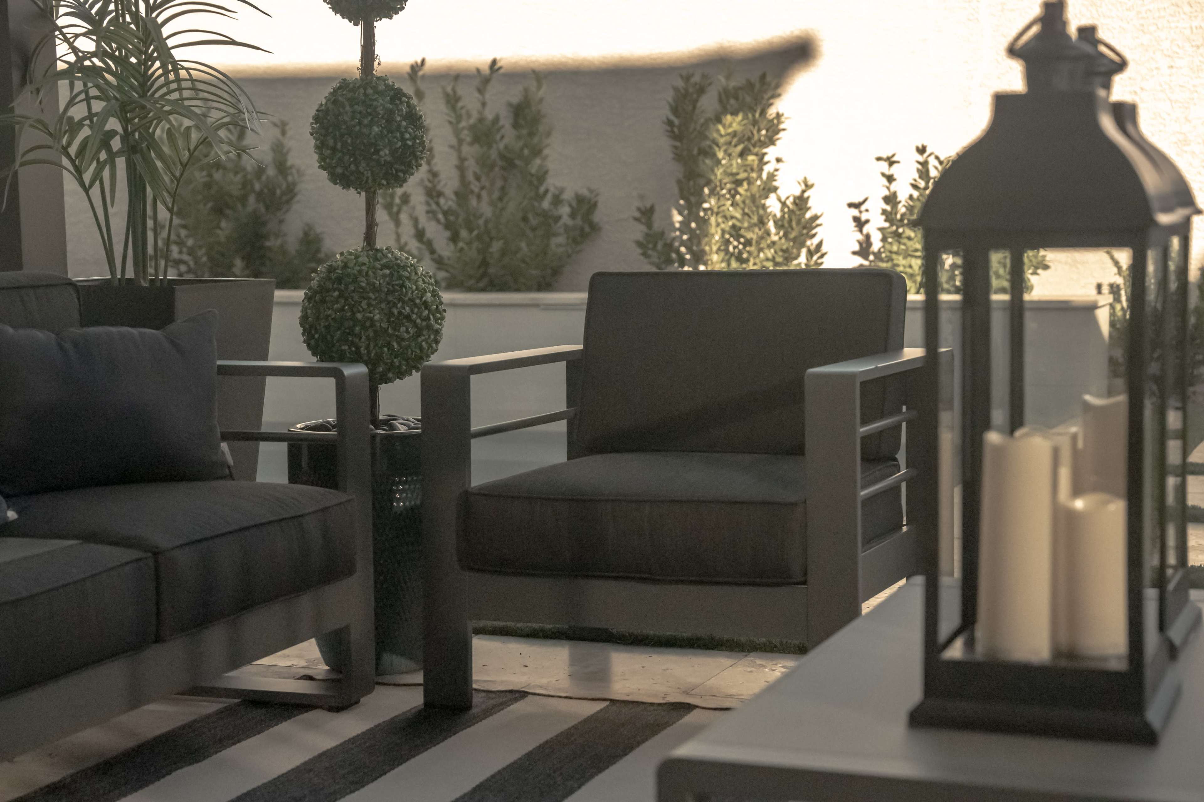 A modern outdoor seating area with potted topiary plants, a lantern, and a striped rug.