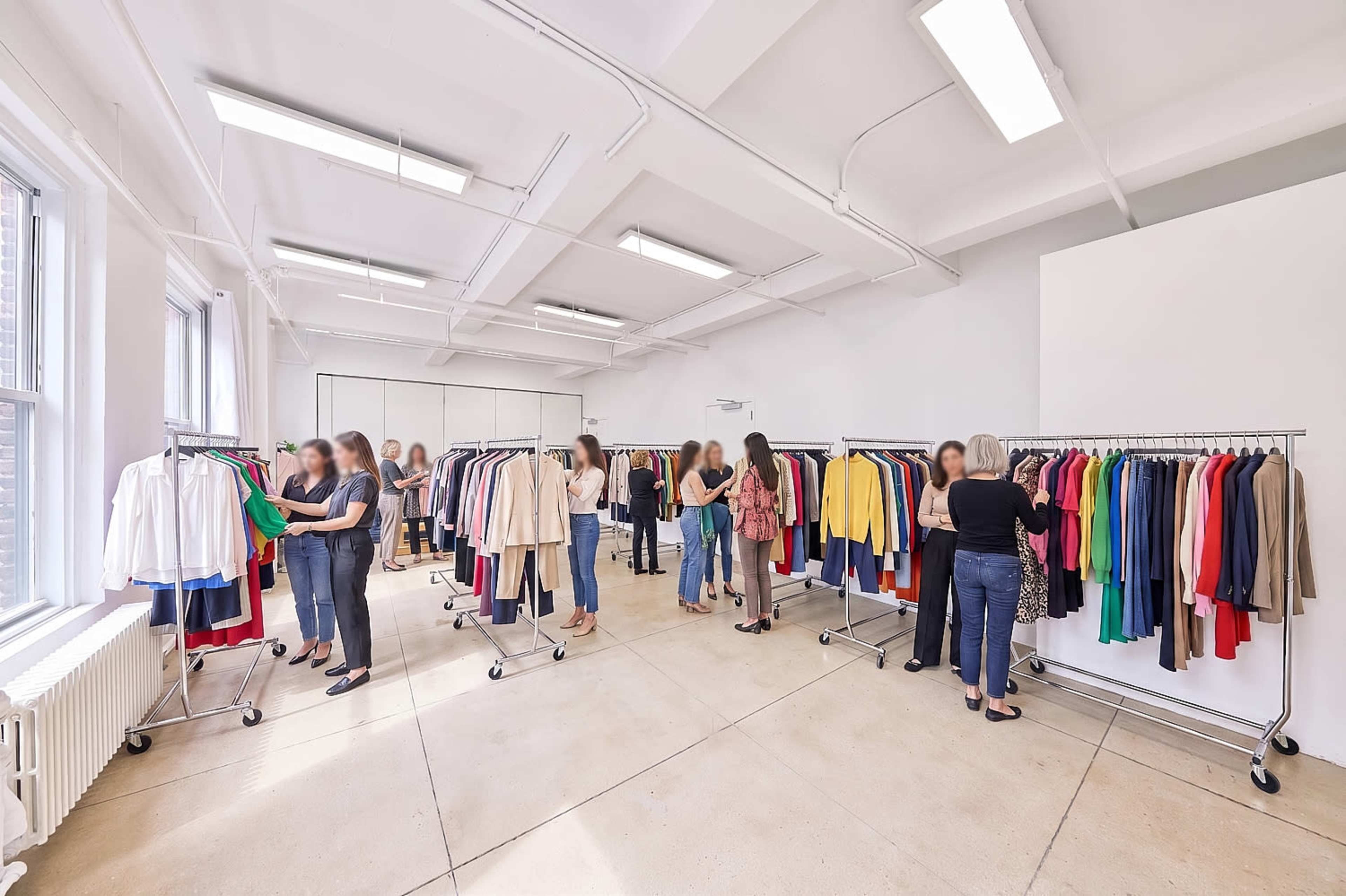A group of people browse and select clothing from racks positioned in a bright, spacious room.