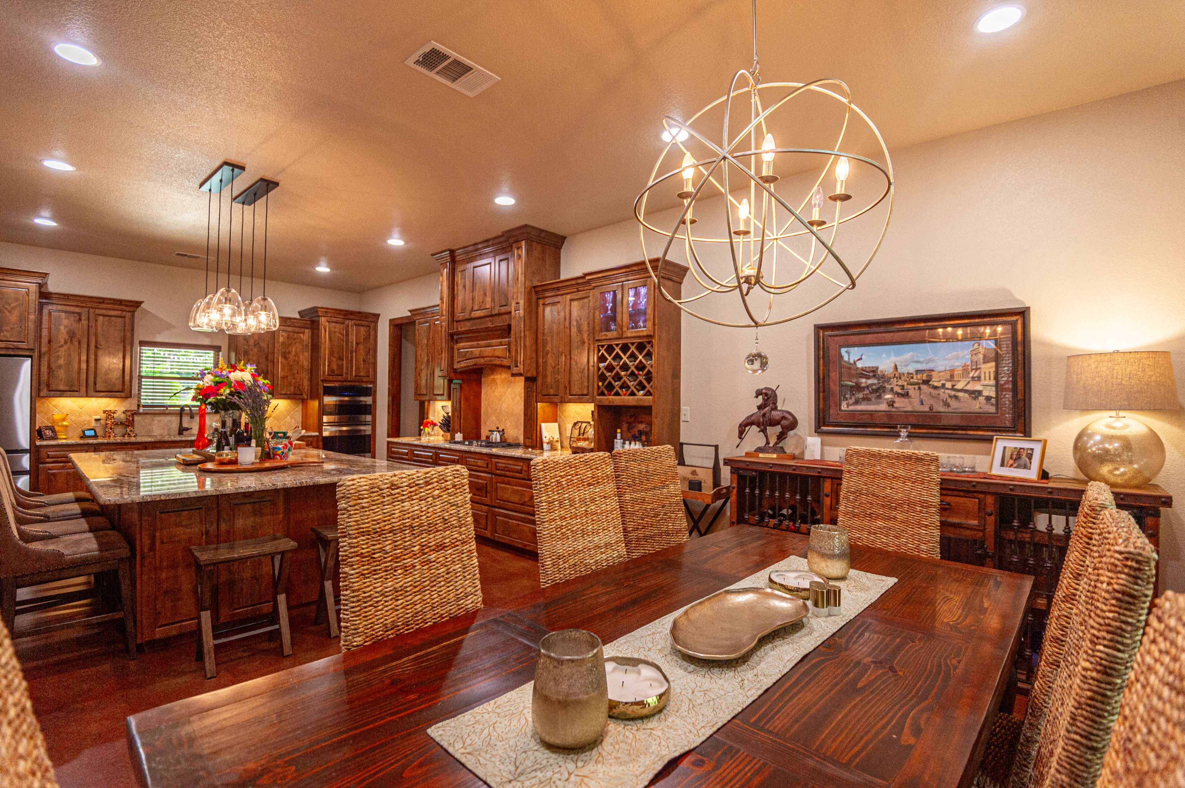 A spacious kitchen and dining area featuring wooden cabinetry, a large dining table with wicker chairs, and modern lighting fixtures.
