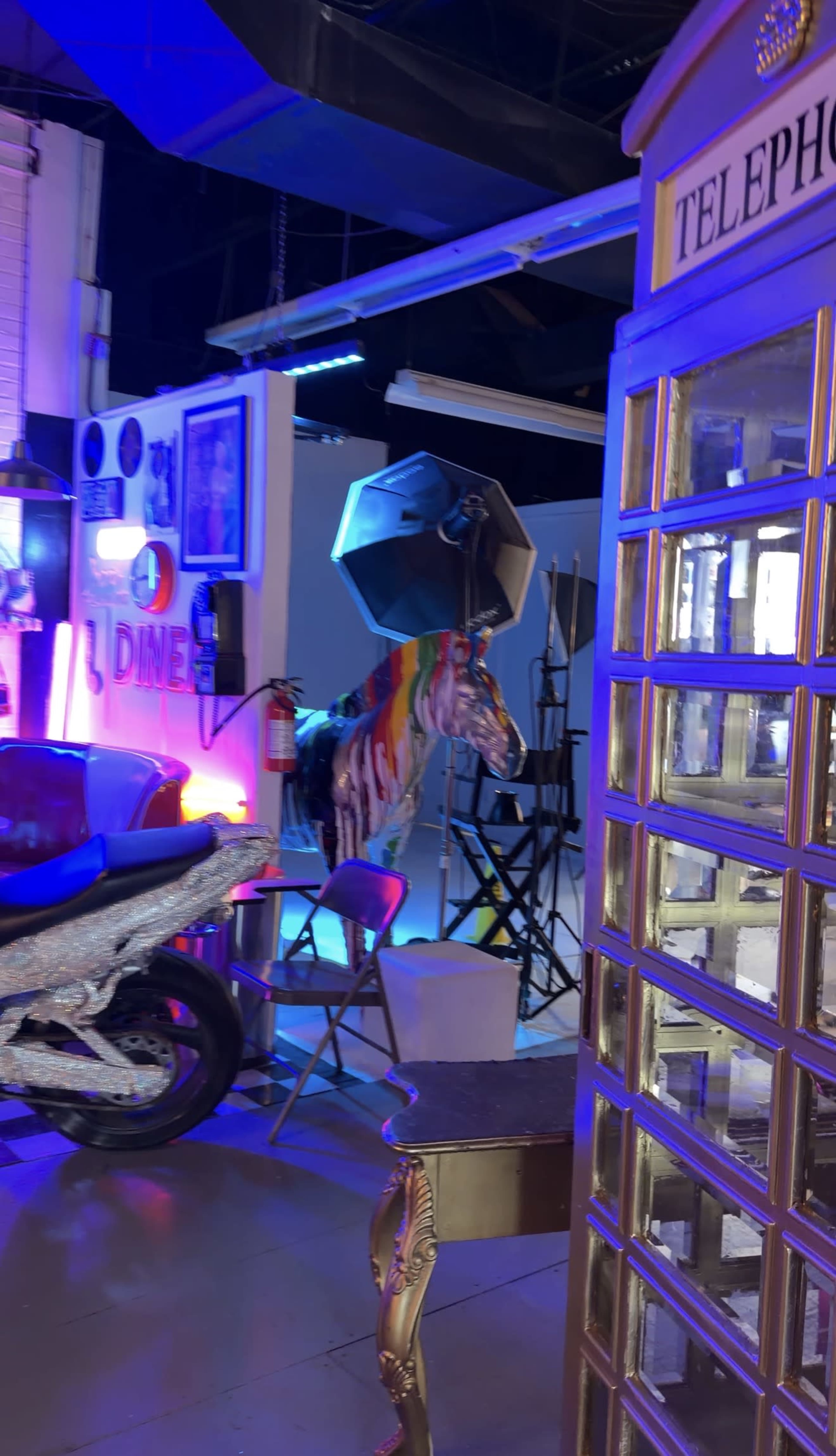 The scene features a colorful diner-themed interior with a motorcycle, a striped horse sculpture, and a vintage telephone booth.