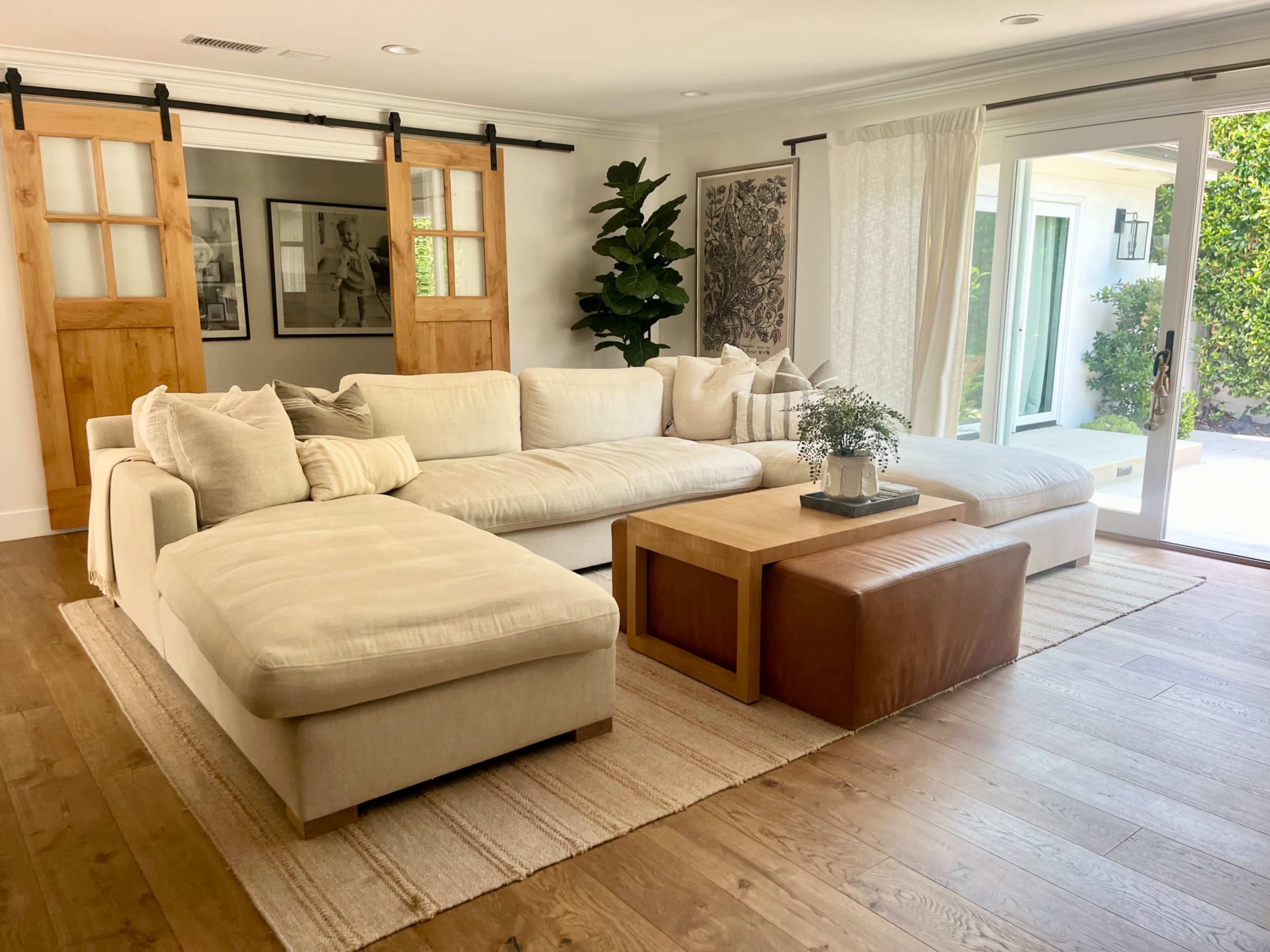 A modern living room featuring a large sectional sofa, a wooden coffee table, and sliding barn doors leading to an outdoor area.