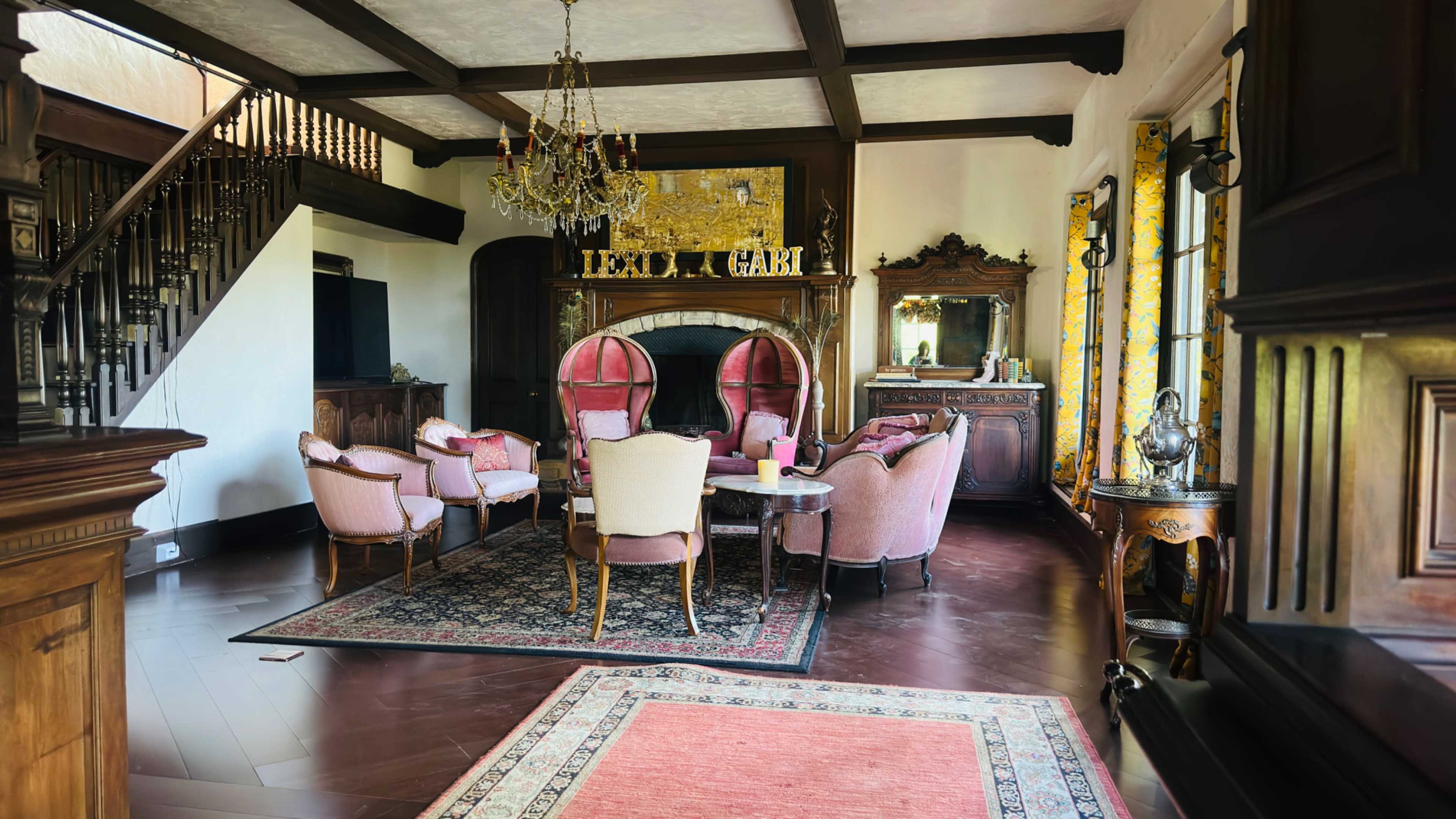 The image shows a beautifully decorated living room featuring a dining area with elegant chairs, a chandelier, and a staircase in the background.