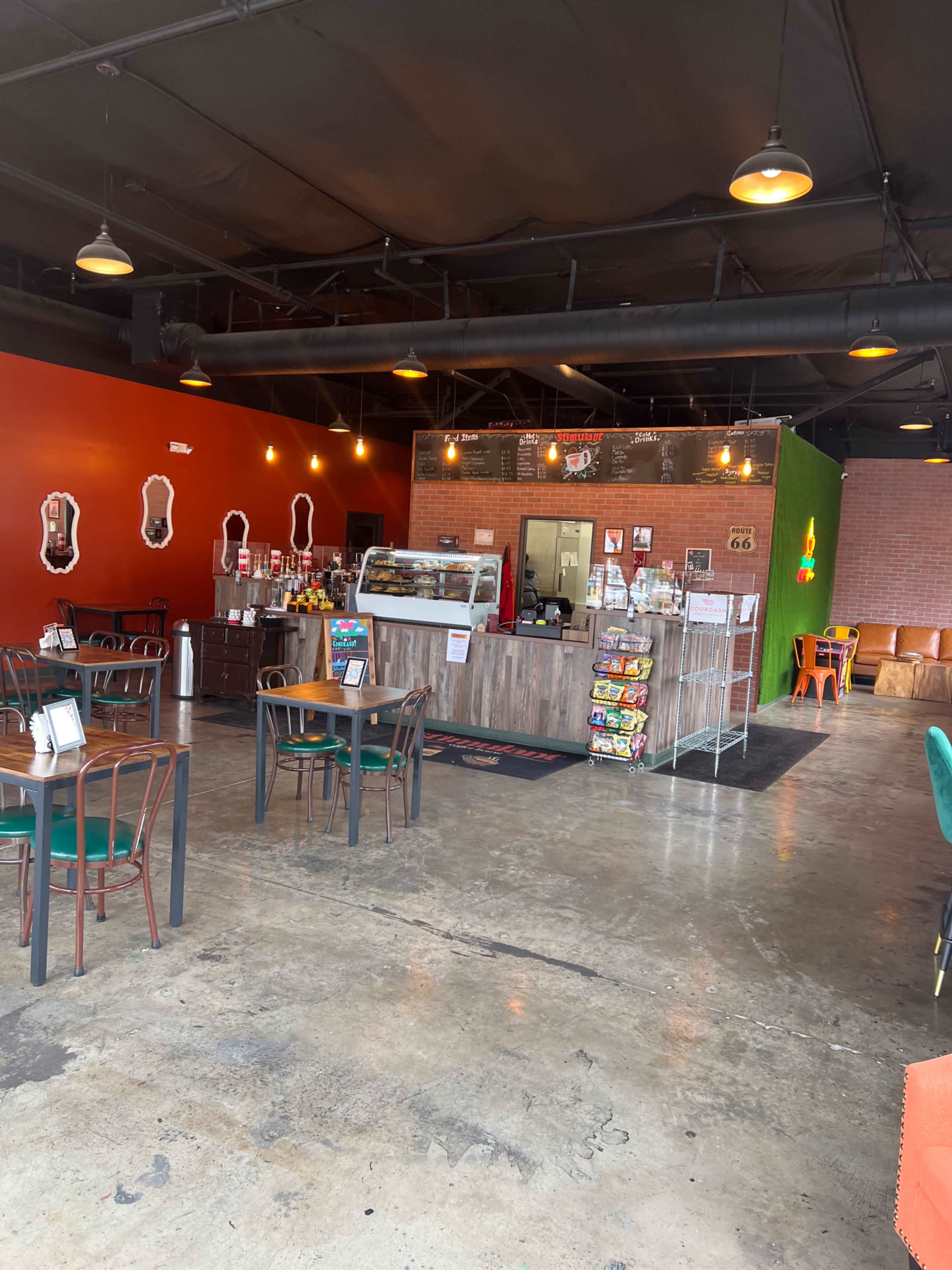 The interior of a cafe featuring a counter with display cases, a seating area with green and black chairs, and a colorful wall.