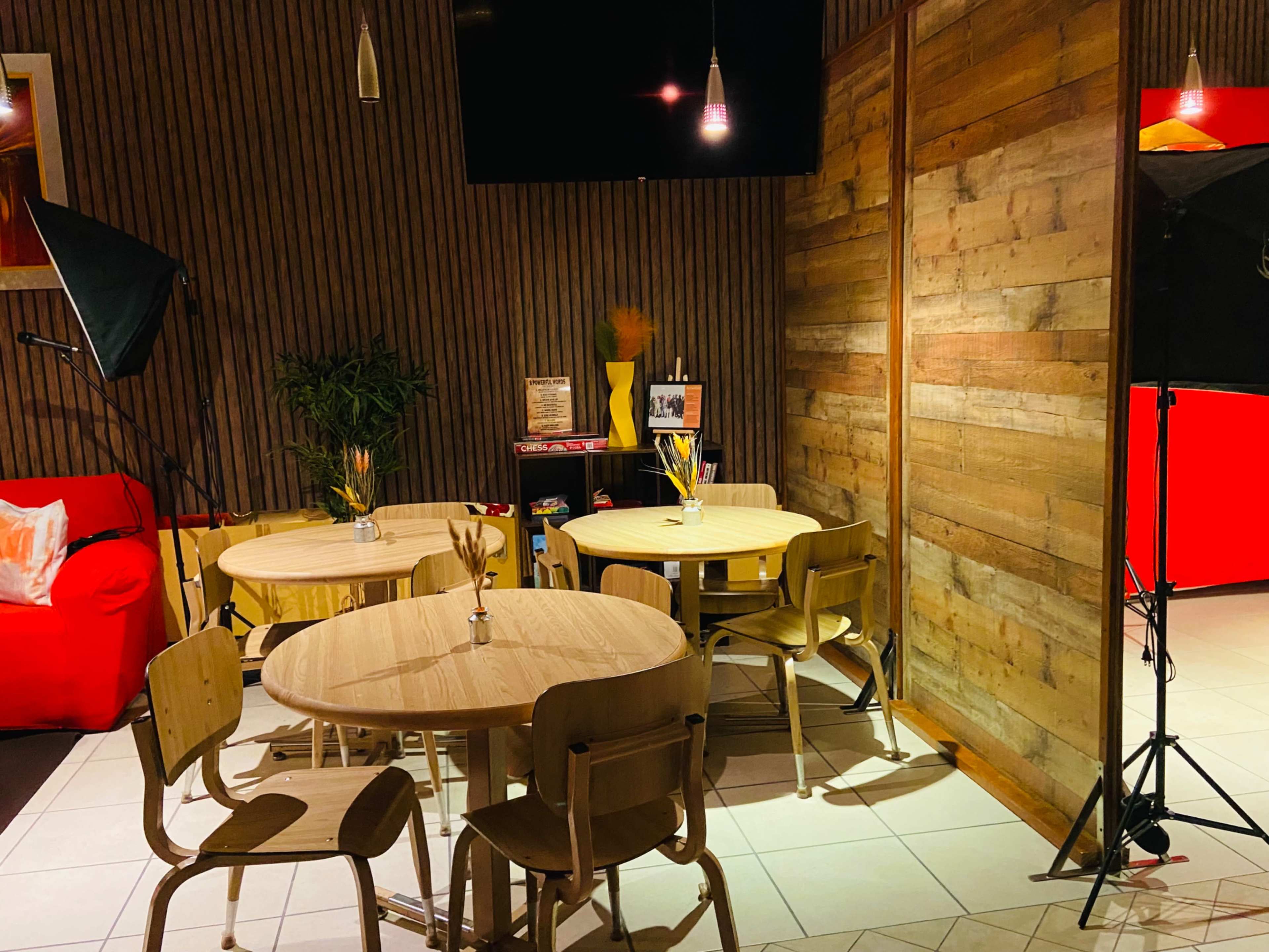 A cozy cafe interior with wooden tables, chairs, and a red couch, separated by a wooden partition and featuring a large television screen.