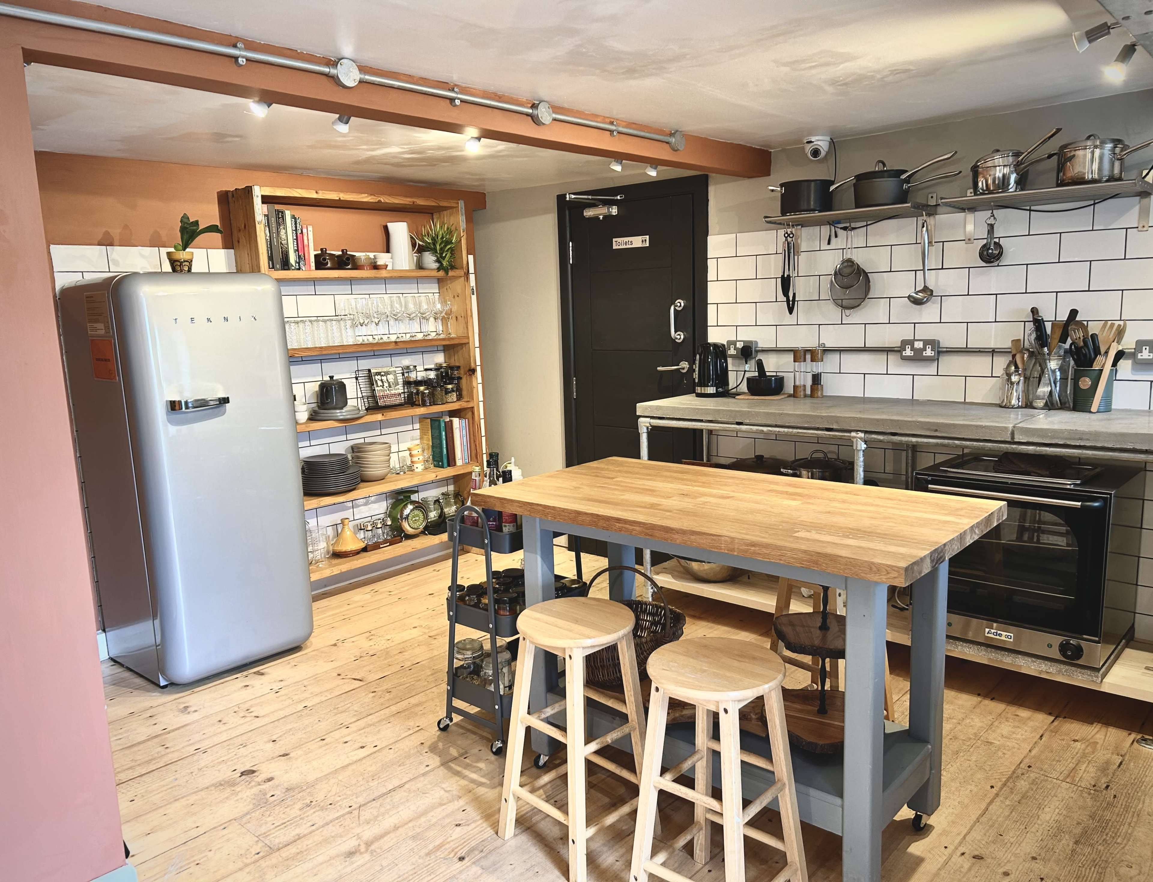 The kitchen features a retro-style refrigerator, a wooden dining table with stools, and open shelving displaying various kitchen items.