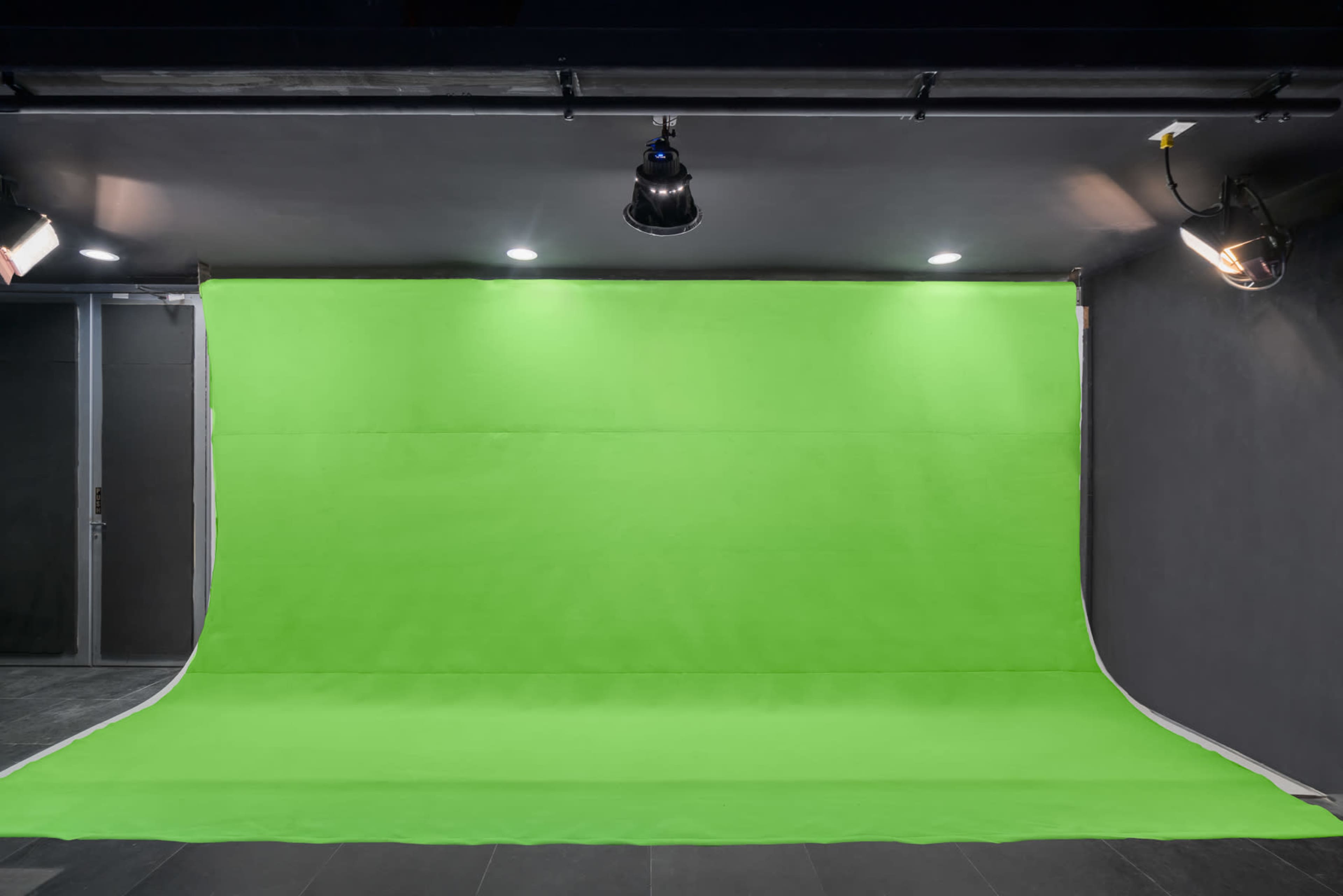 A photography studio with a large green backdrop and multiple lights positioned above.