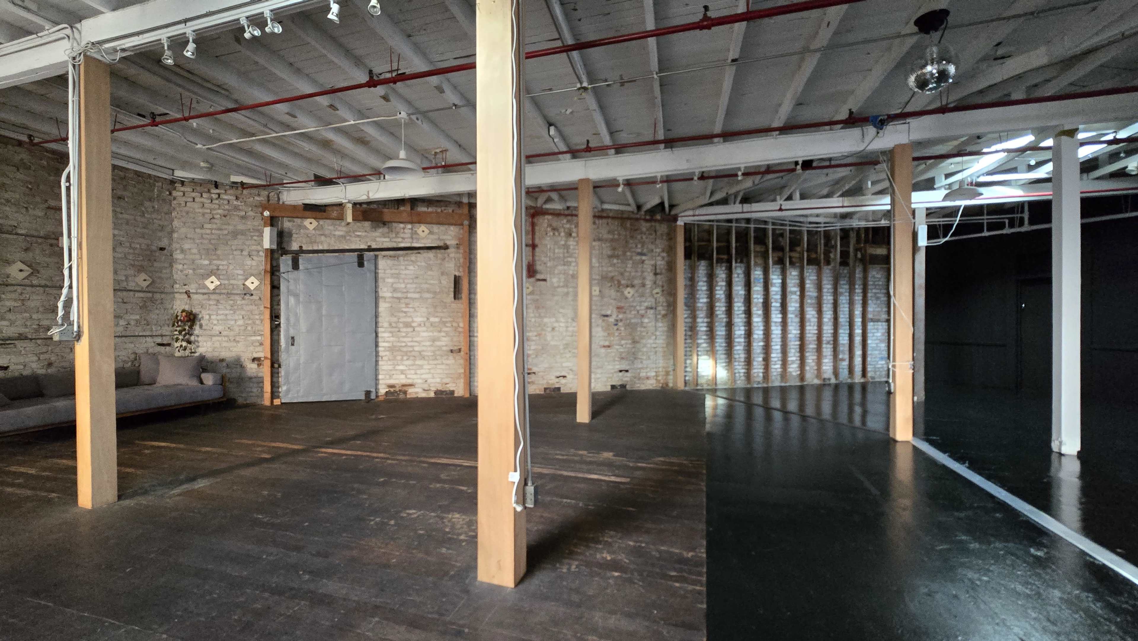 An empty industrial space with wooden pillars, exposed brick walls, and a curved black floor section.