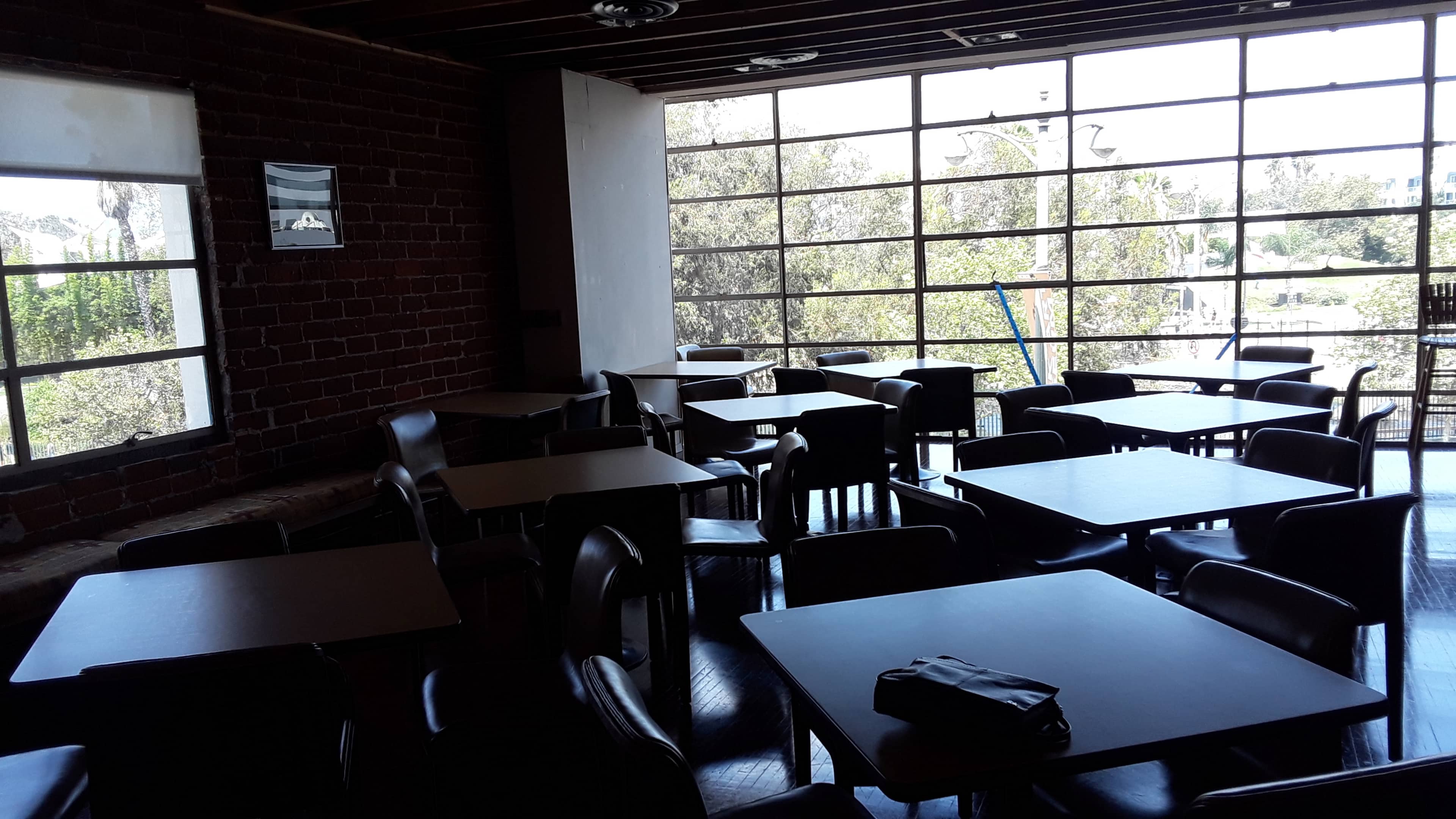 An empty café space with several small tables and chairs arranged in front of large windows.