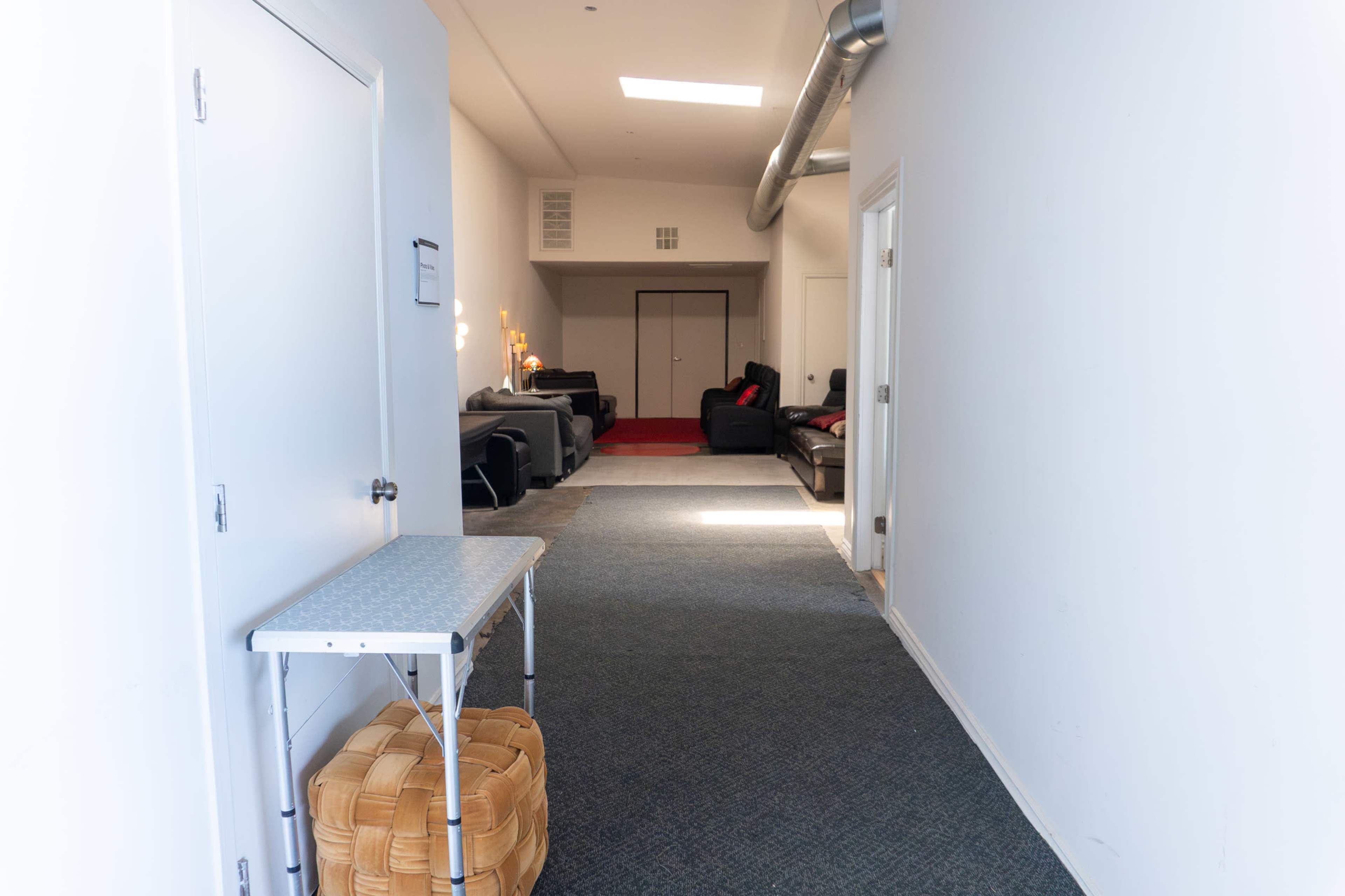 The image shows a hallway leading to a living area with couches and a red carpet.