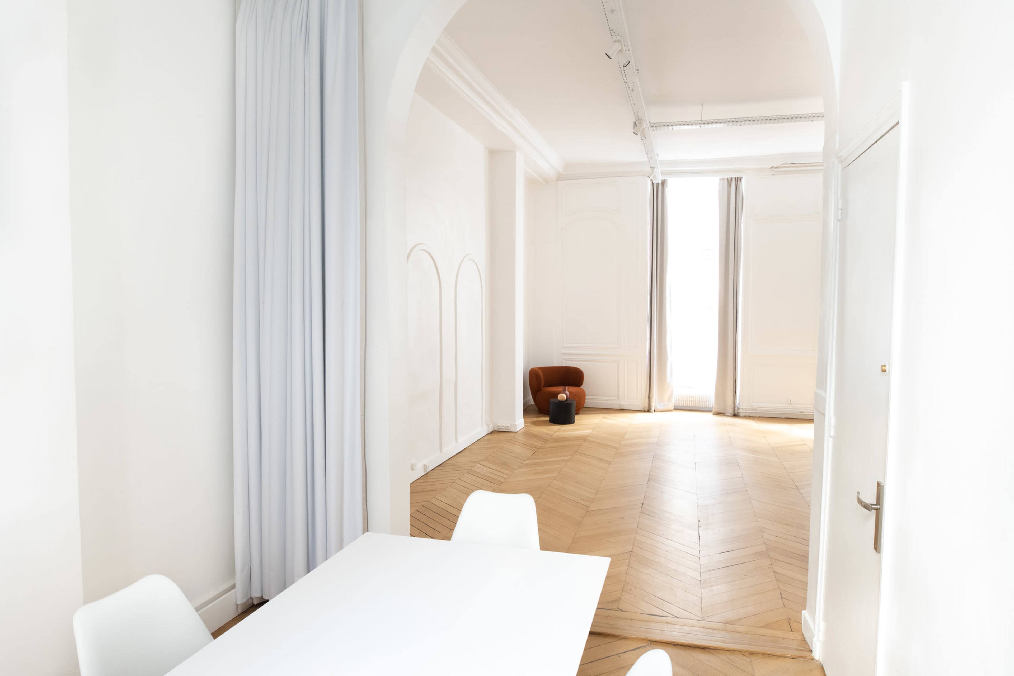 A spacious room with light-colored walls, hardwood flooring, and large windows draped with curtains.