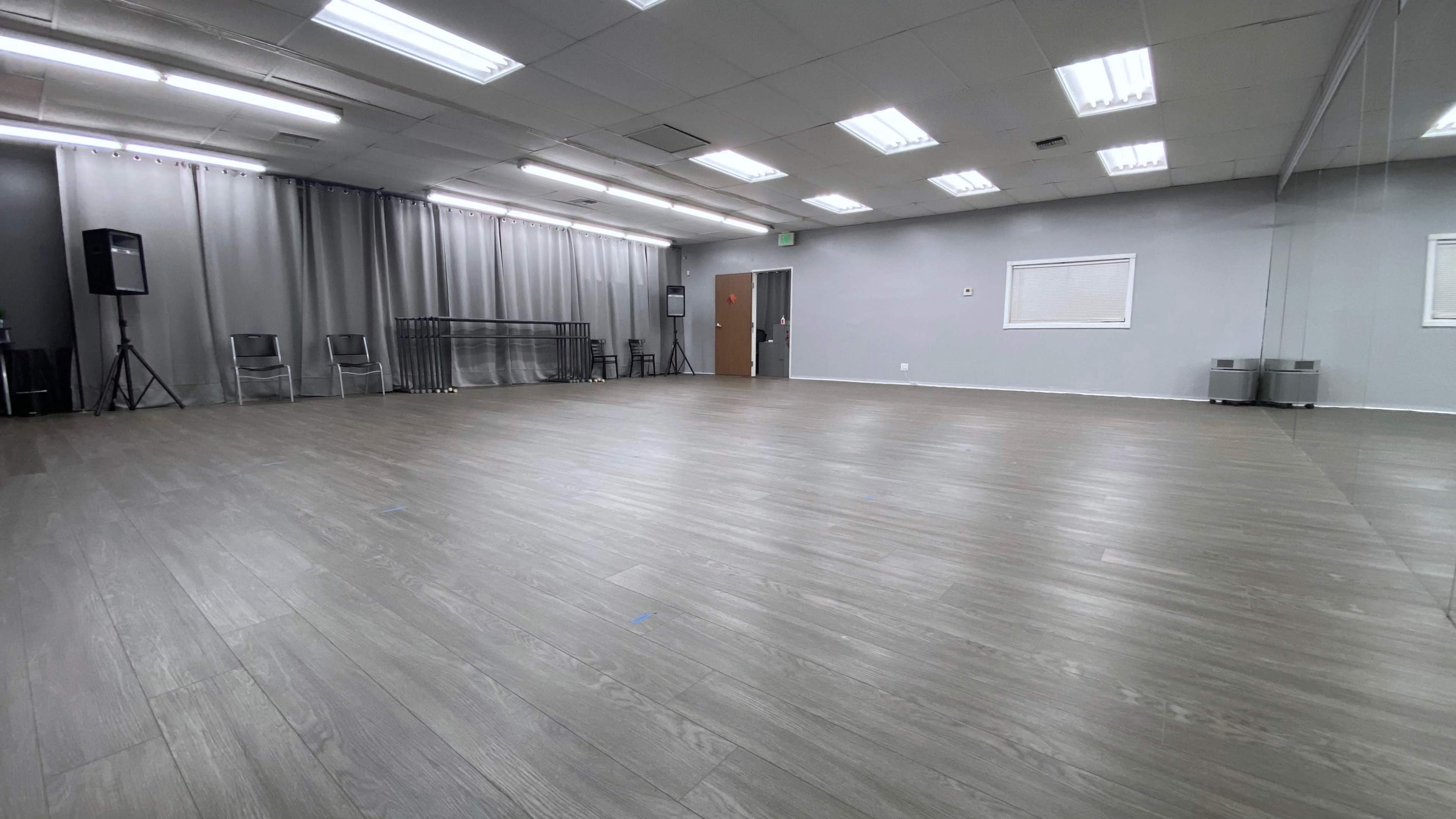 An empty dance studio with wooden flooring, gray walls, and a large mirror on one side.