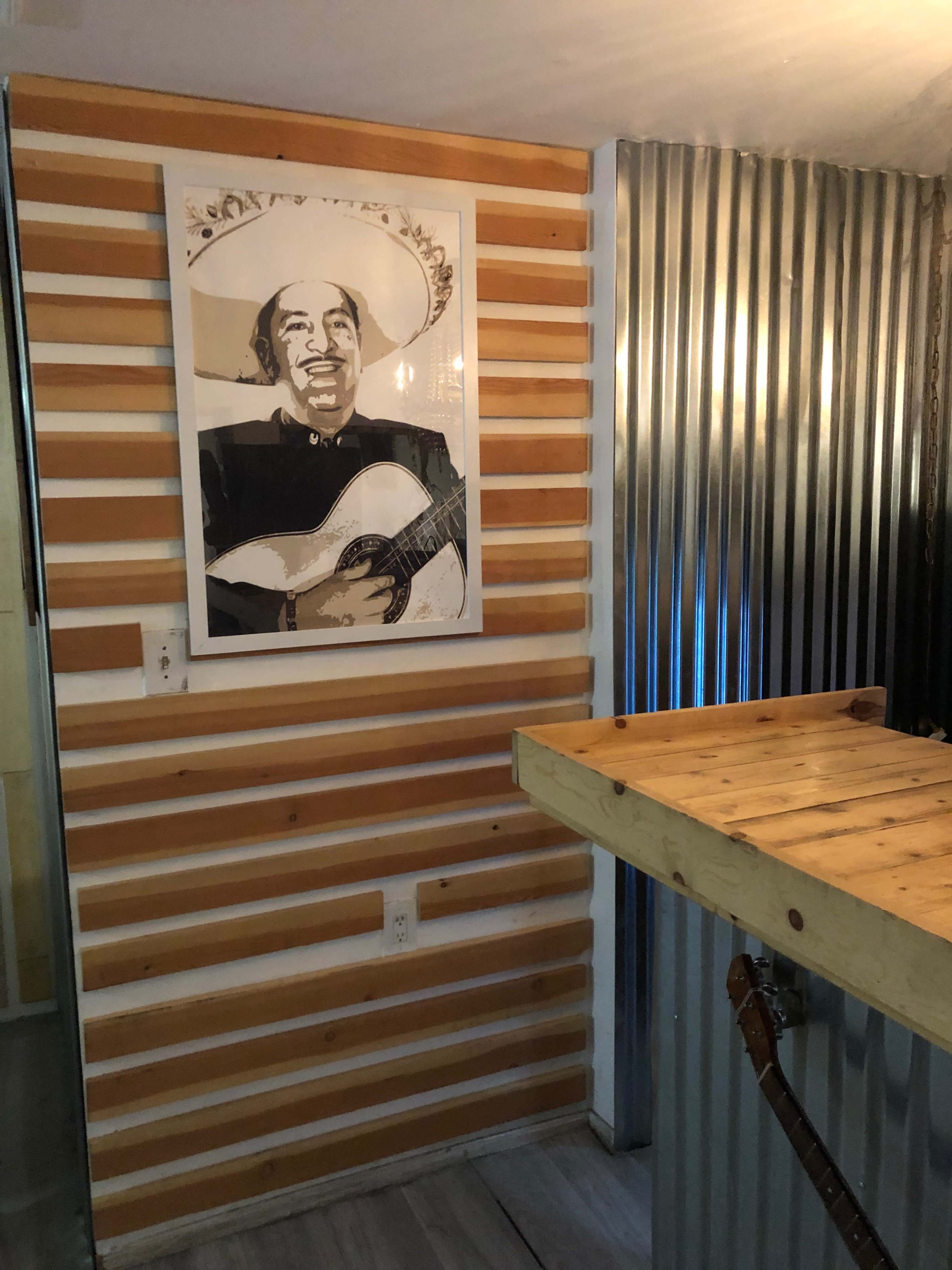A modern interior with a wooden wall featuring a framed portrait of a man playing guitar, alongside a corrugated metal section and a wooden bar.