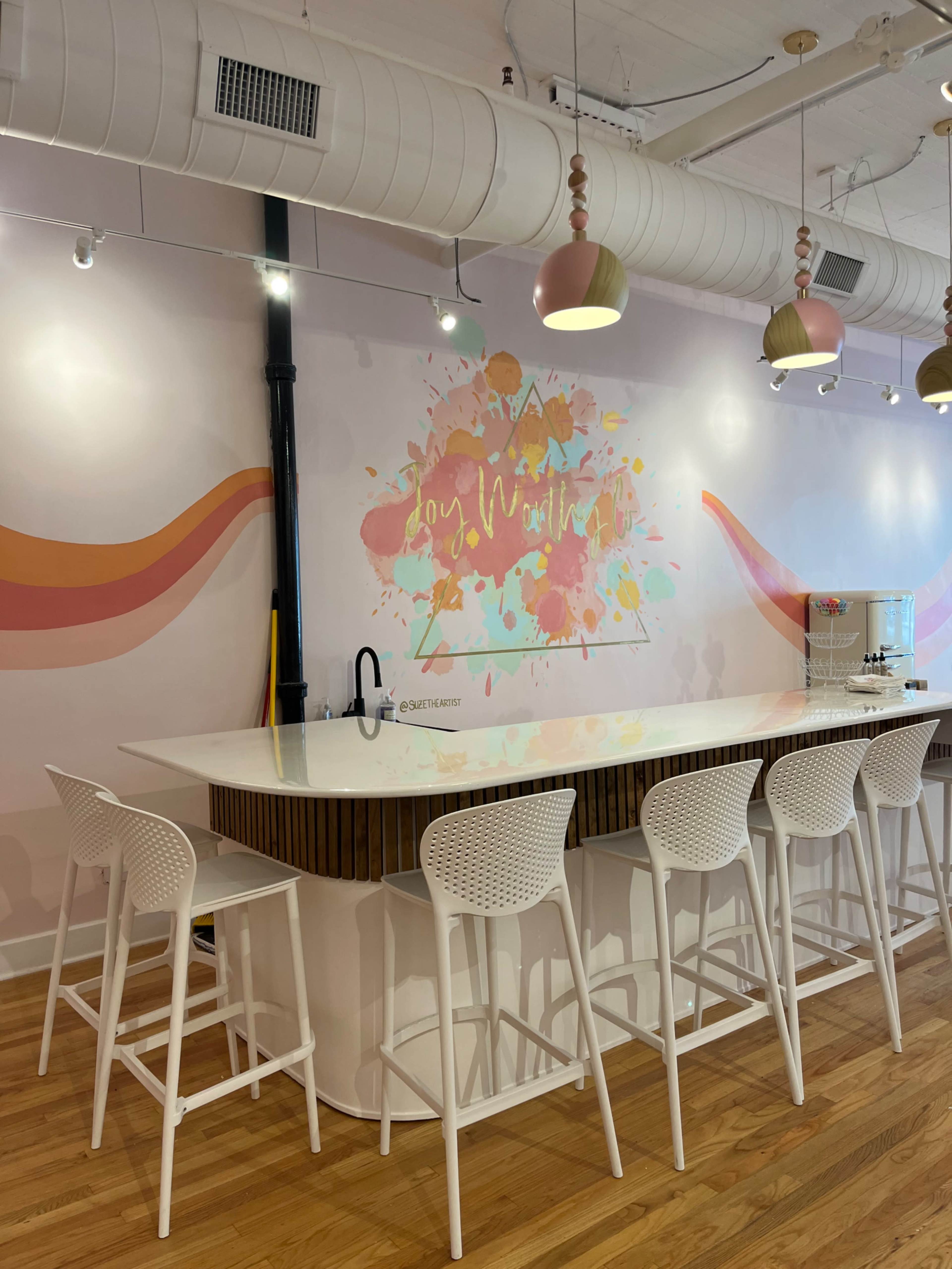 A bright and modern café interior features a white countertop with high stools and a colorful mural on the wall.