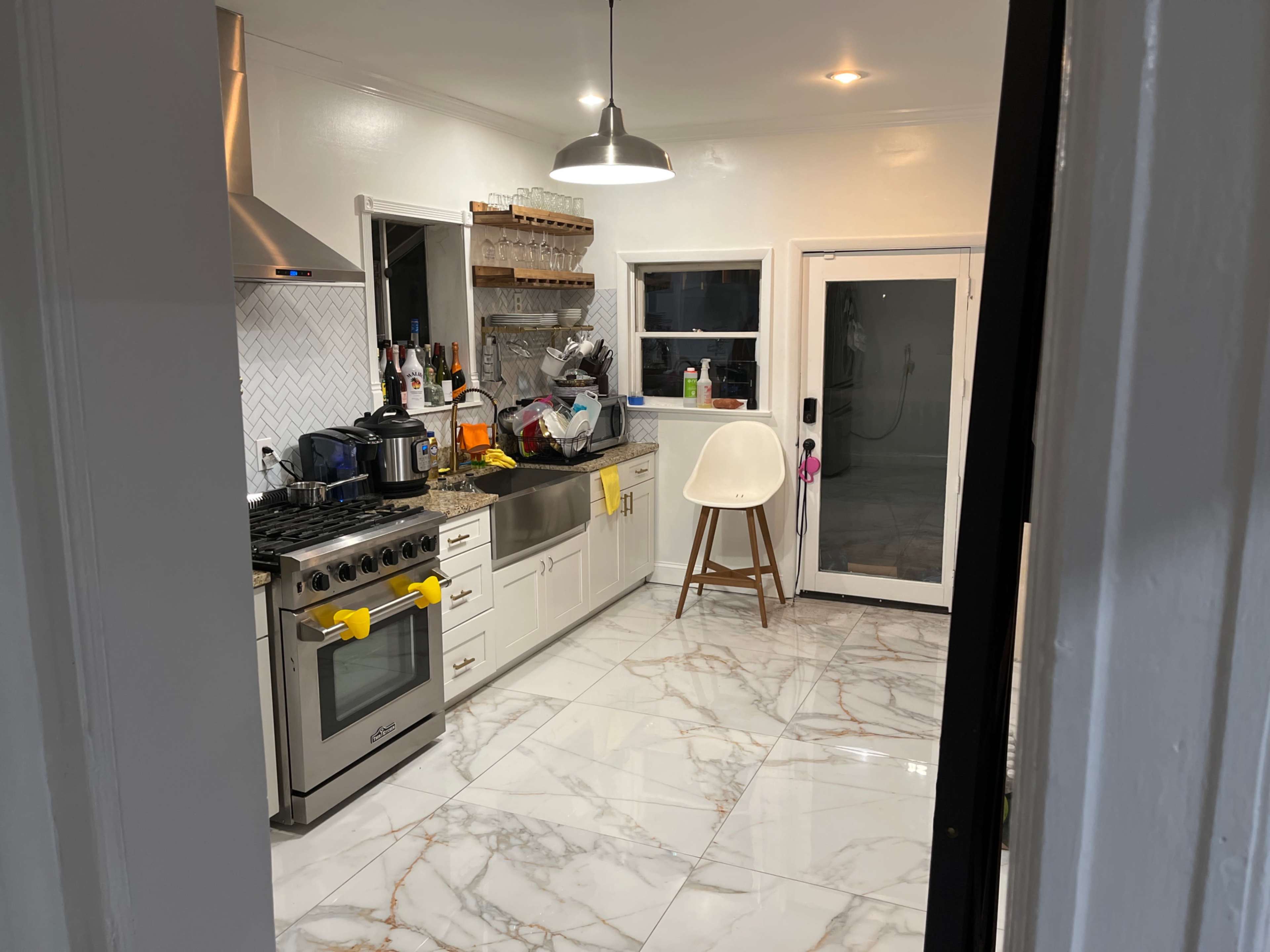 A modern kitchen features a large island, stainless steel appliances, and marble flooring with a view of a glass door leading to an outdoor space.