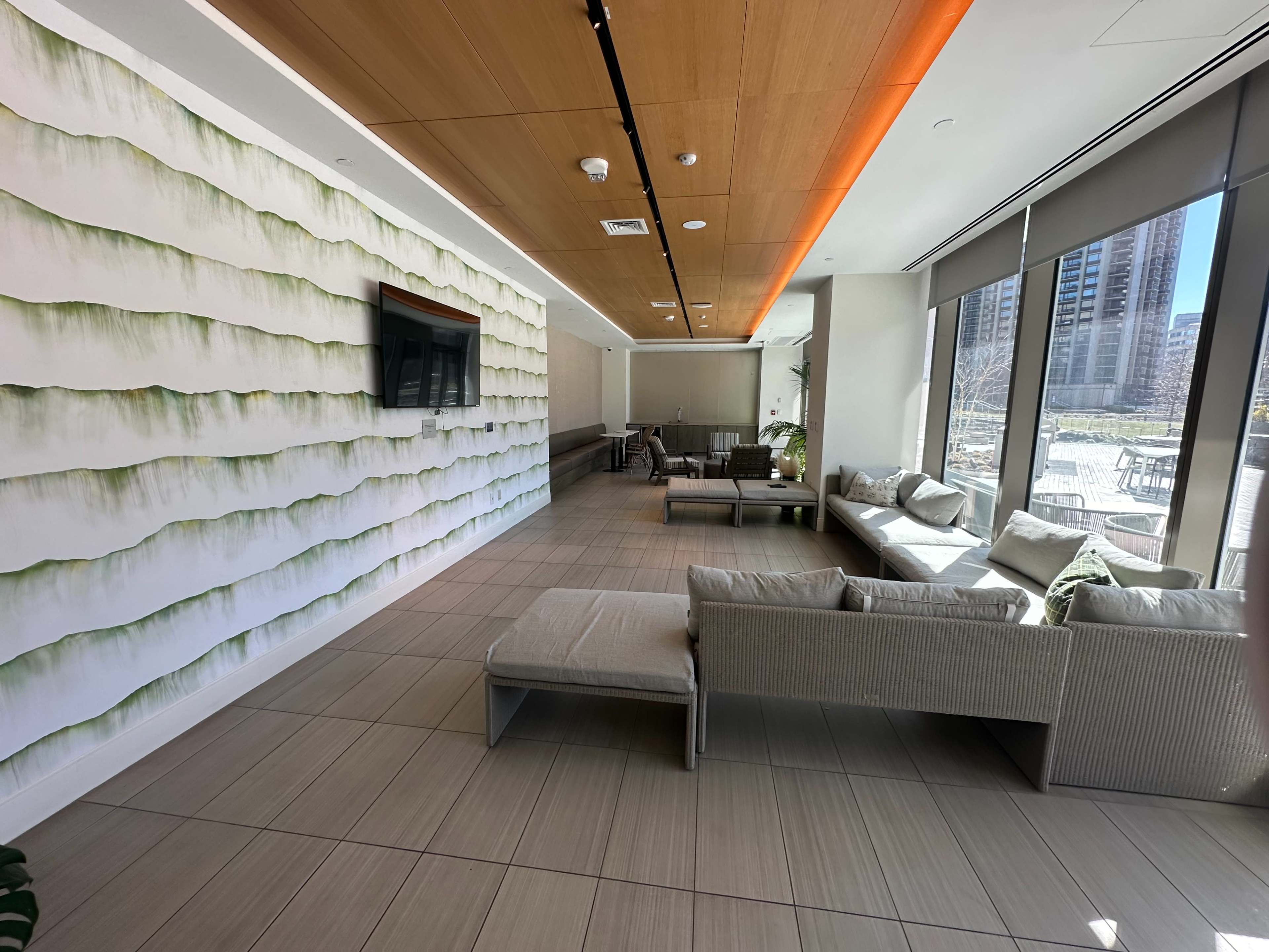 A spacious room with a textured green and white wall, a large television, and several seating arrangements facing a window.