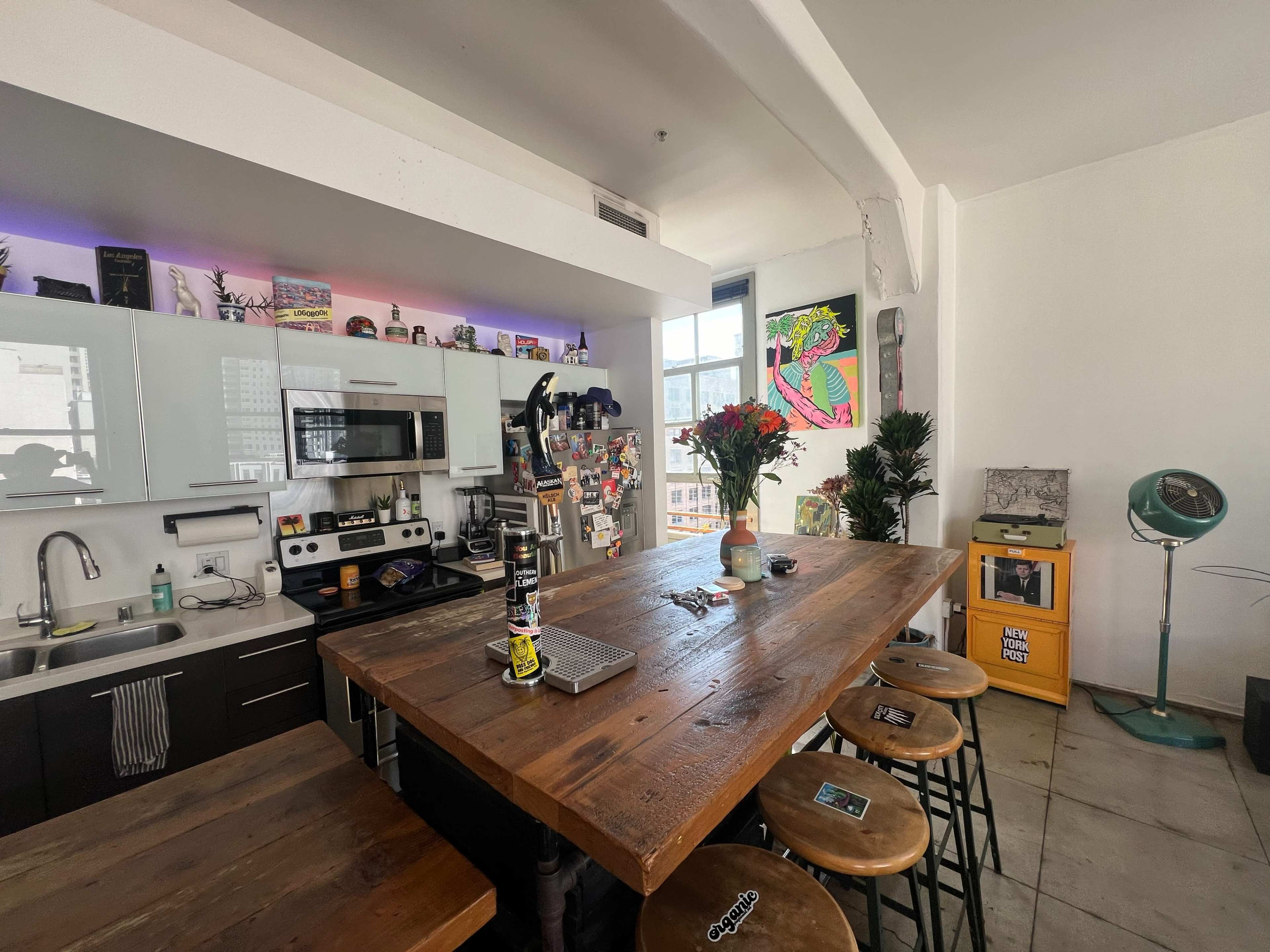 A modern kitchen with a large wooden counter, stools, and various decorative items on the walls and shelves.