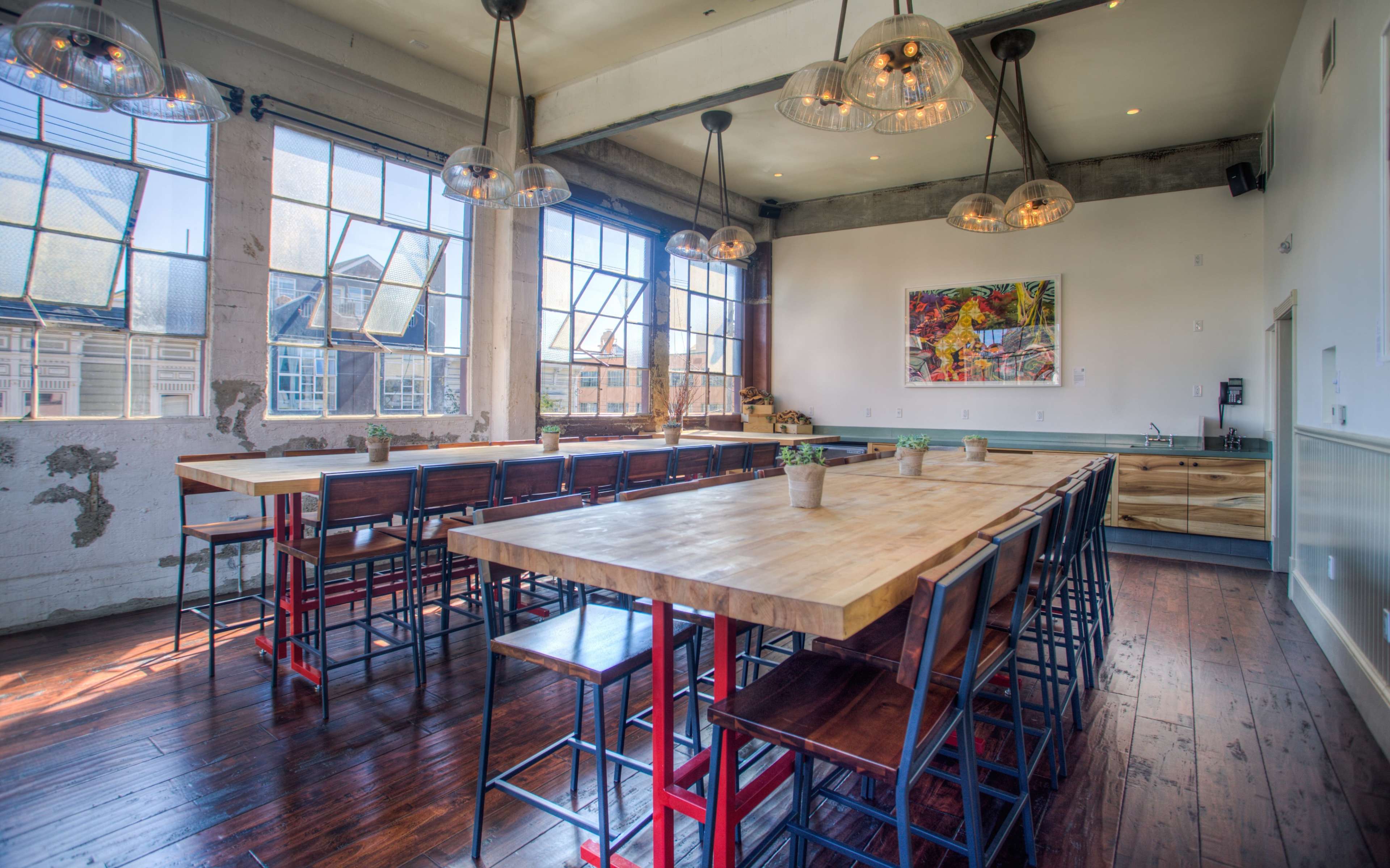 A spacious dining area features large windows, wooden tables with metal stools, and an artistic wall display.